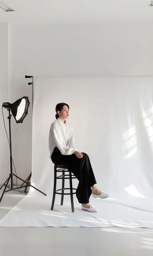 A woman sitting on a stool in front of a white backdrop.
