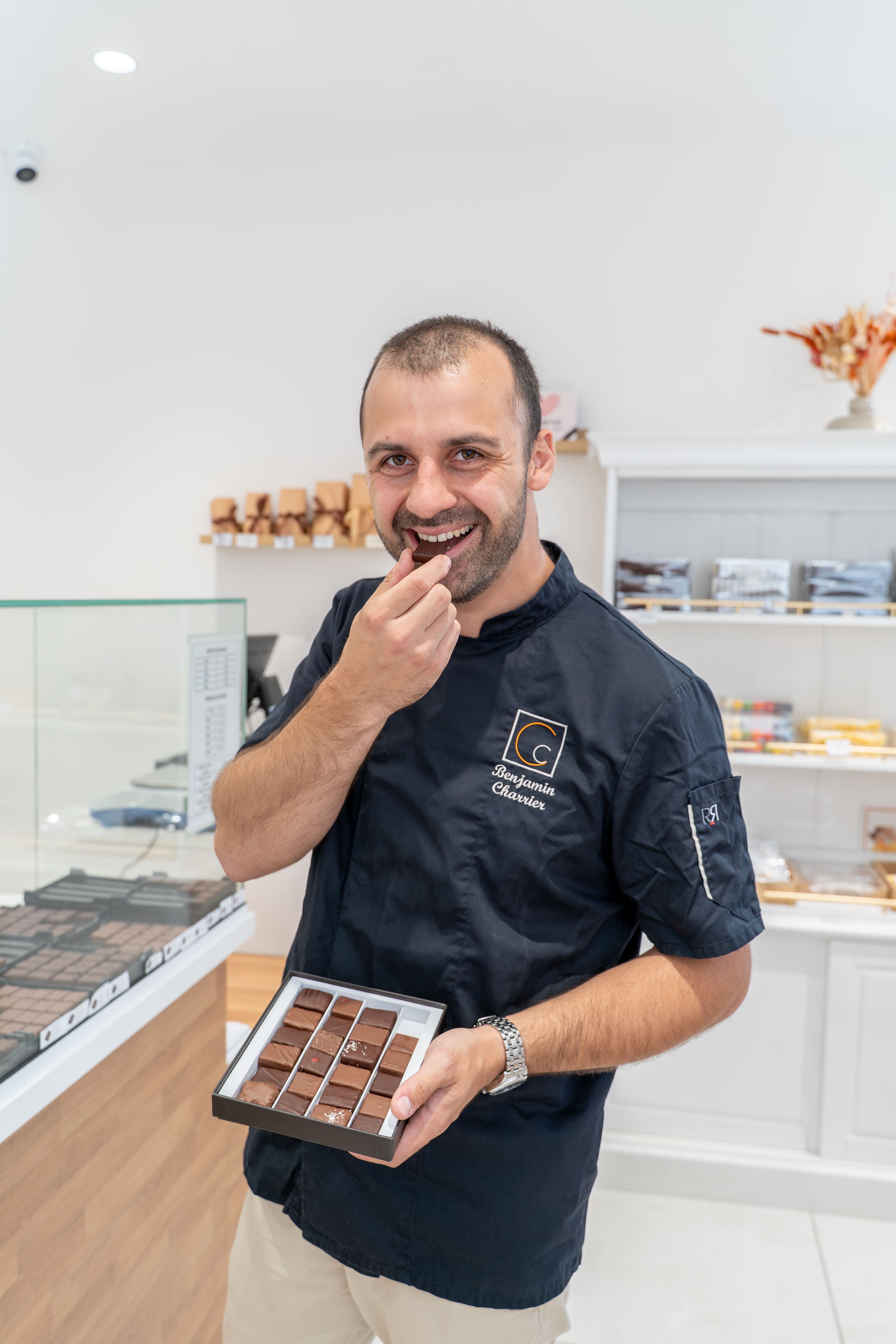 Benjamin Charrier, Maître chocolatier de la Maison Charrier dégustant une création artisanale tout en présentant un coffret de chocolats.