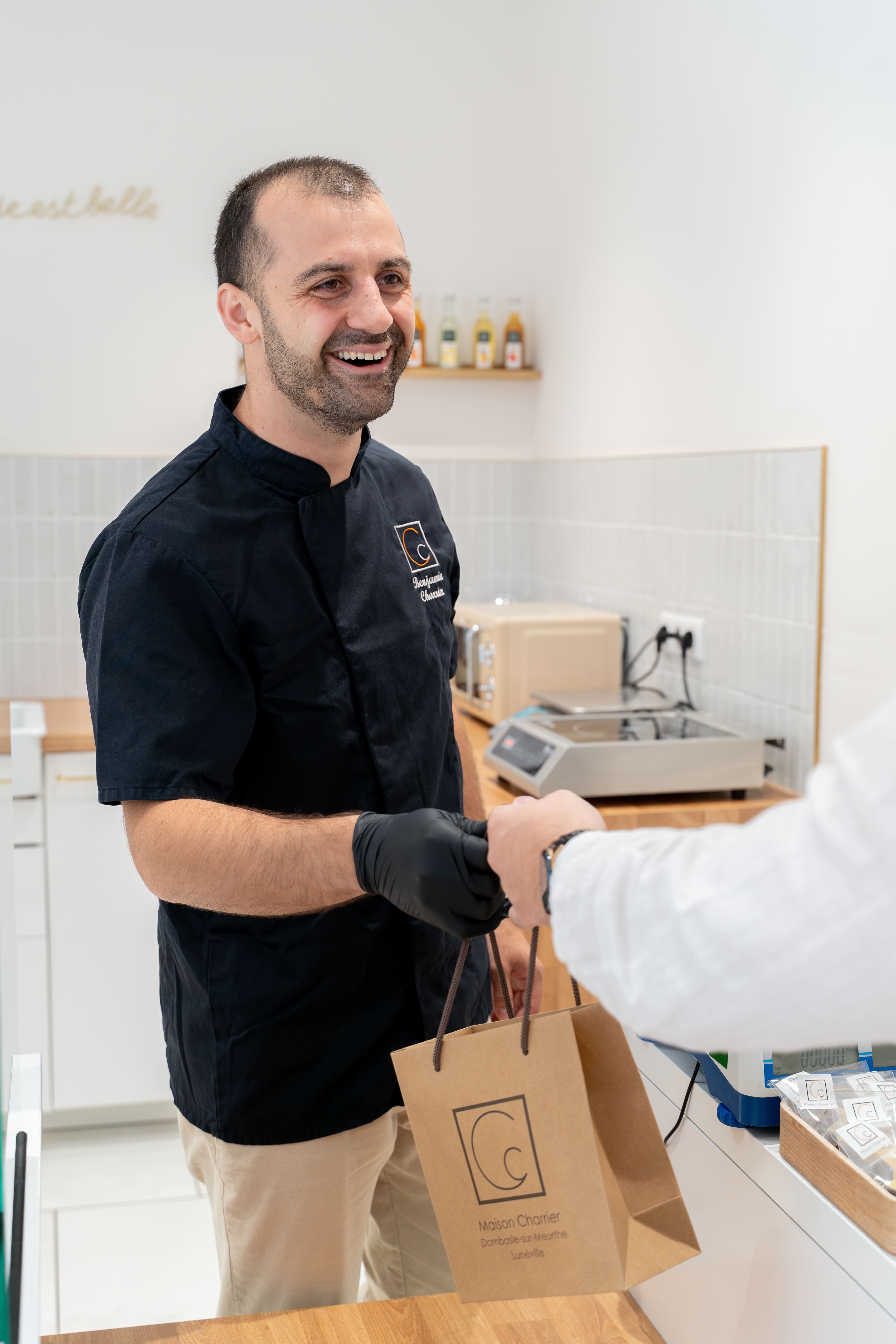 Benjamin Charrier, Maître chocolatier de la Maison Charrier, remettant un sac kraft de chocolats artisanaux à un client dans la boutique de Lunéville.