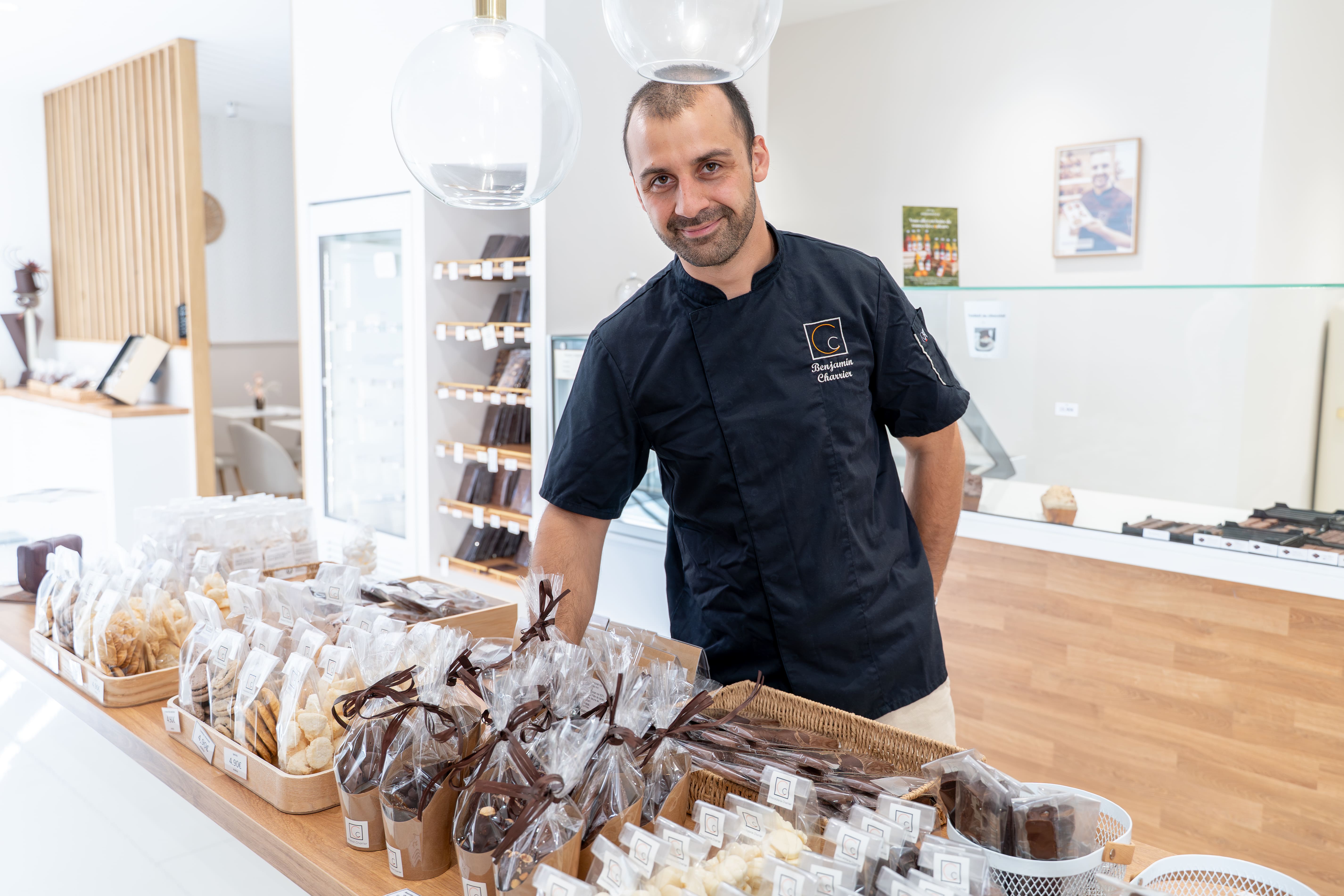 Benjamin Charrier, Maître chocolatier de la Maison Charrier, dans la boutique de Lunéville, devant un étal de créations artisanales en chocolat emballés.