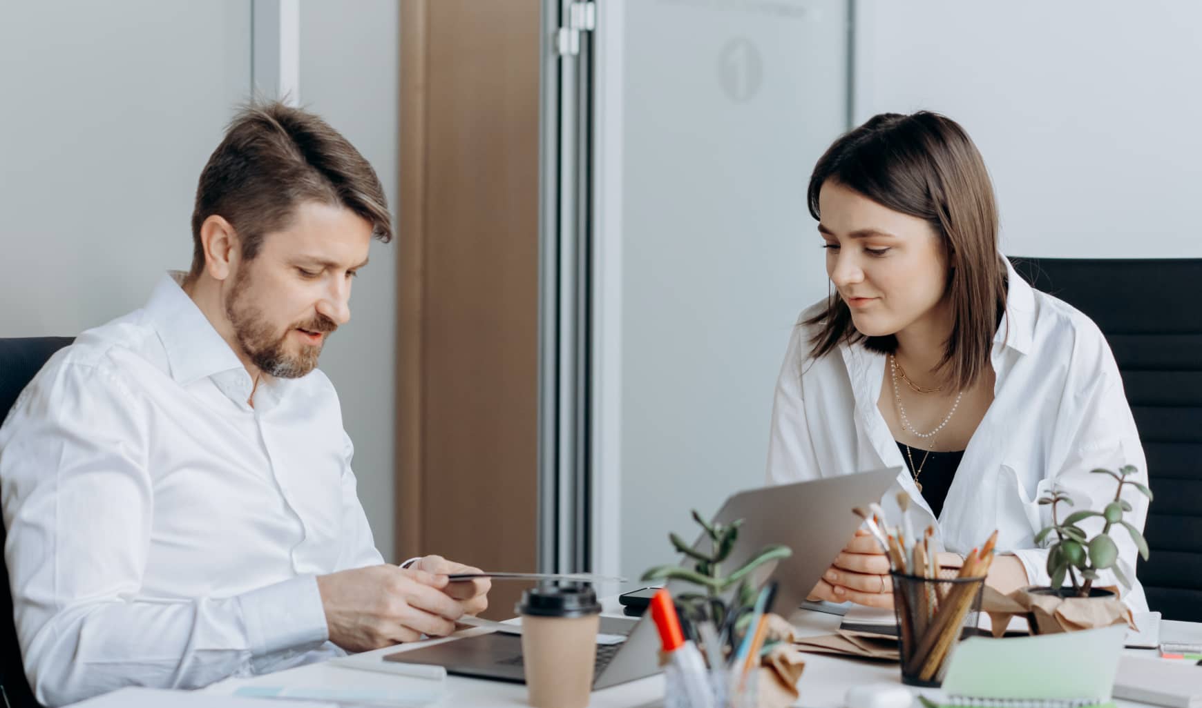 A man and woman sitting at a desk looking at a tablet.