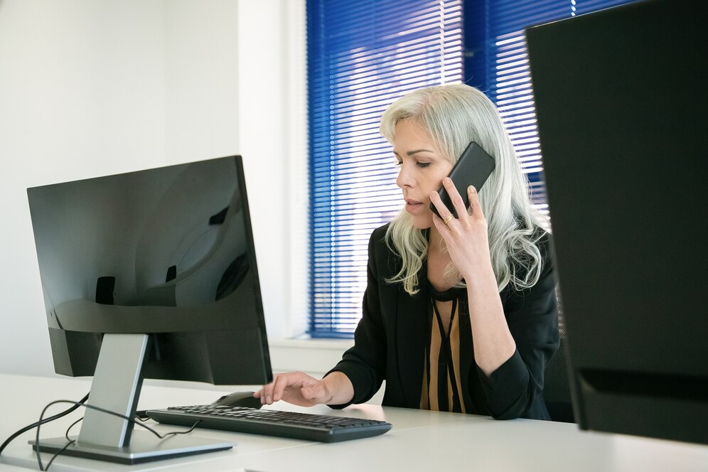 A woman sitting at a desk talking on a cell phone.
