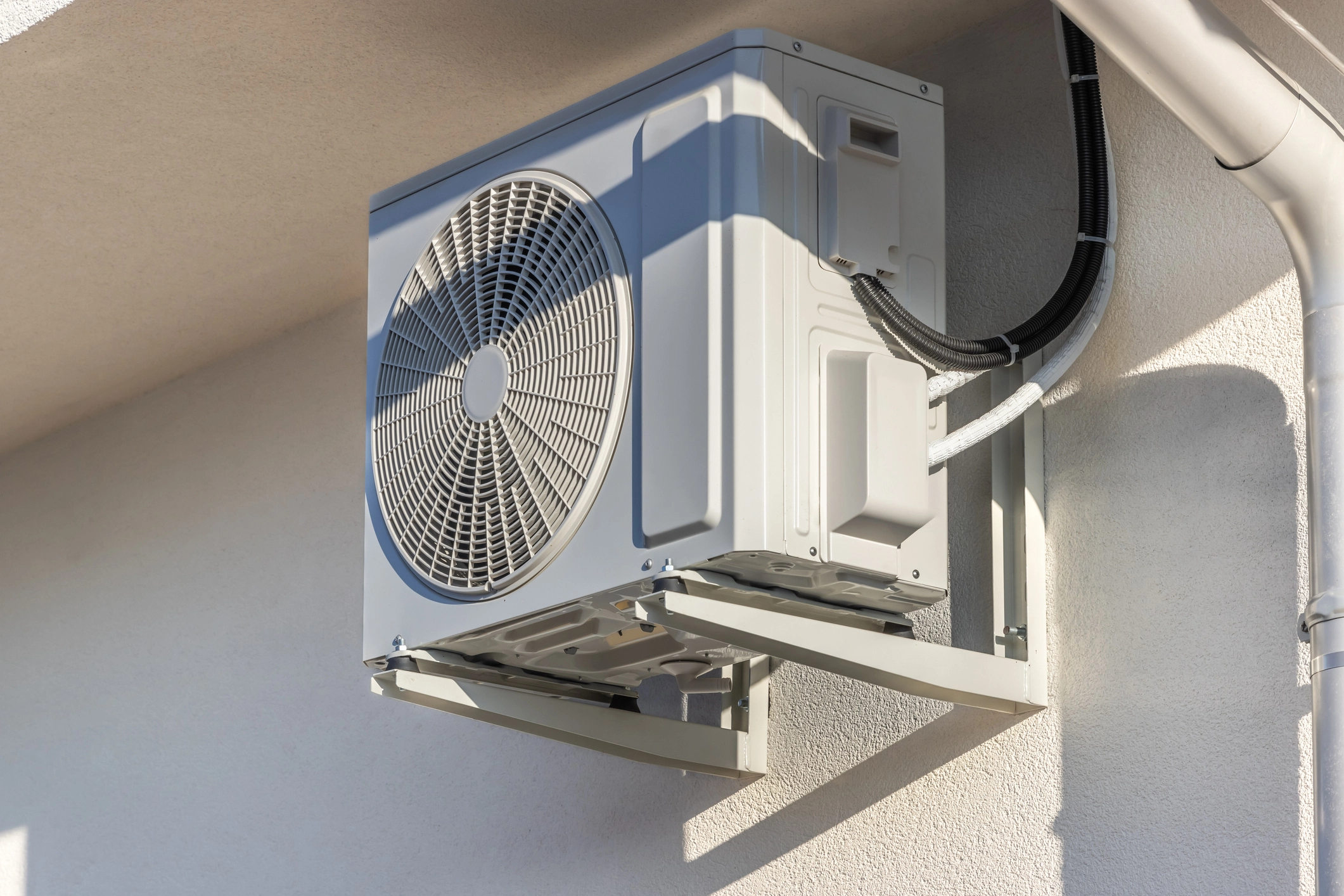 Modern white outdoor air conditioning condenser unit mounted on a building wall