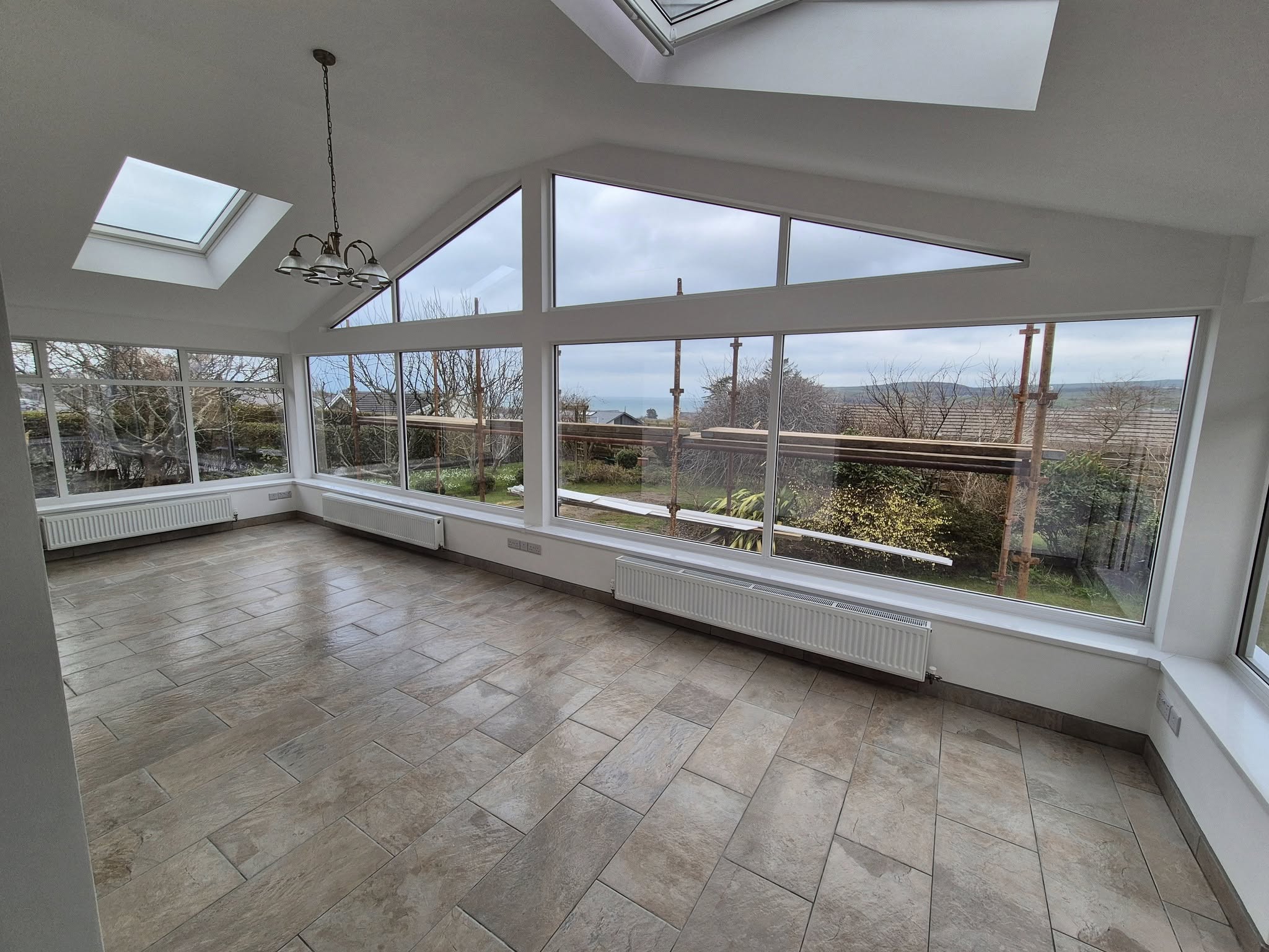 A bright, modern room with large windows and a skylight, showing freshly plastered and finished interior walls.
