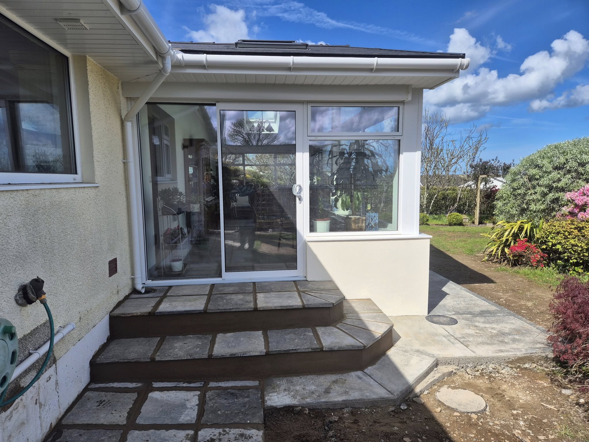 Exterior of extension with large windows and patio, blue sky above.