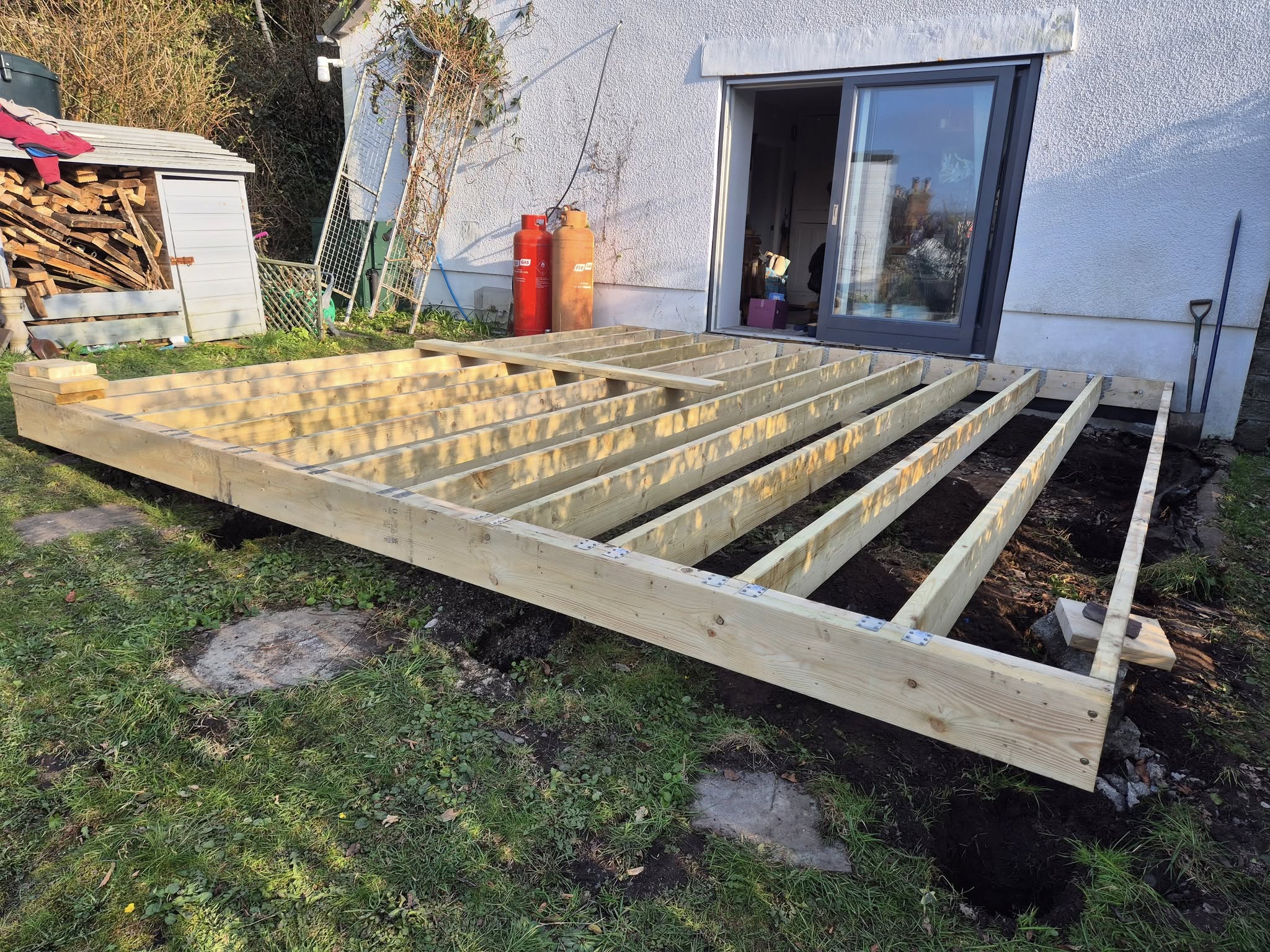 Timber frame for new decking, part-built beside a white house.