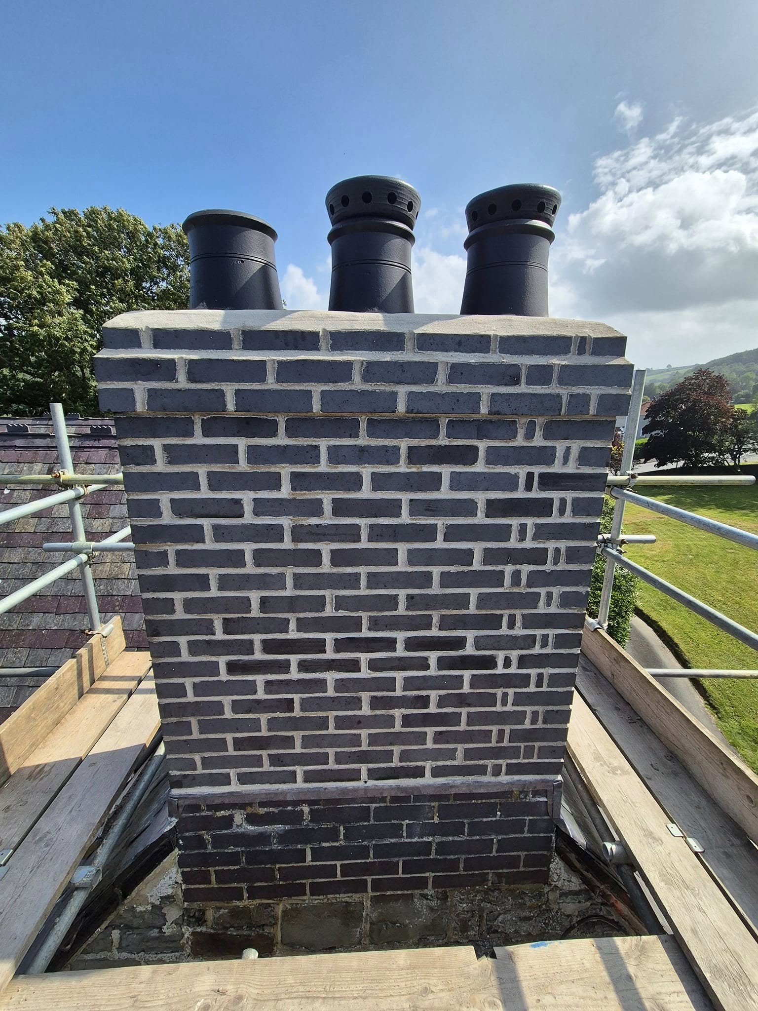 Three newly finished brick chimney stacks in a row on a tiled roof.
