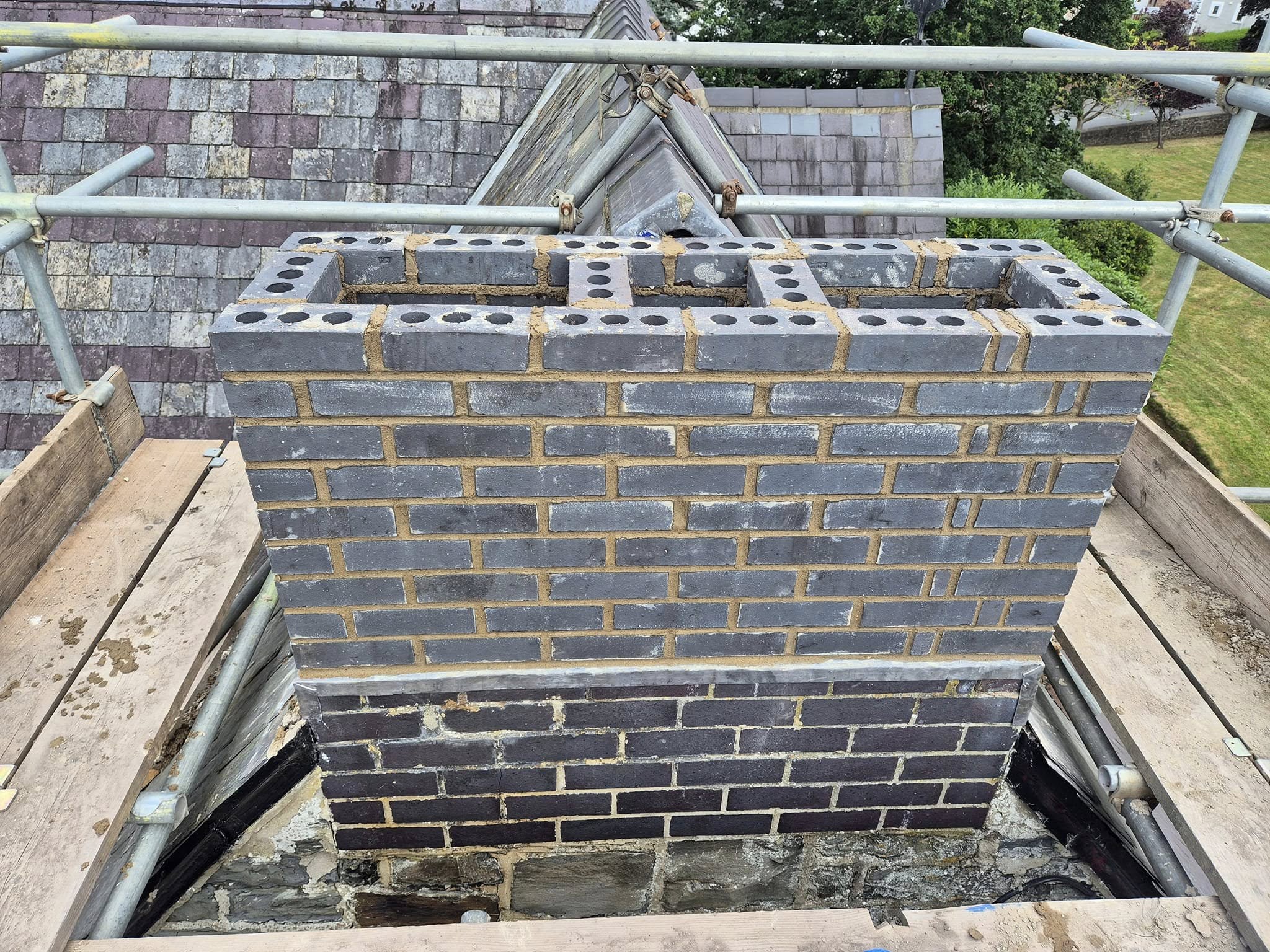 View along a roof with multiple chimneys, showing roof tiles and scaffold.