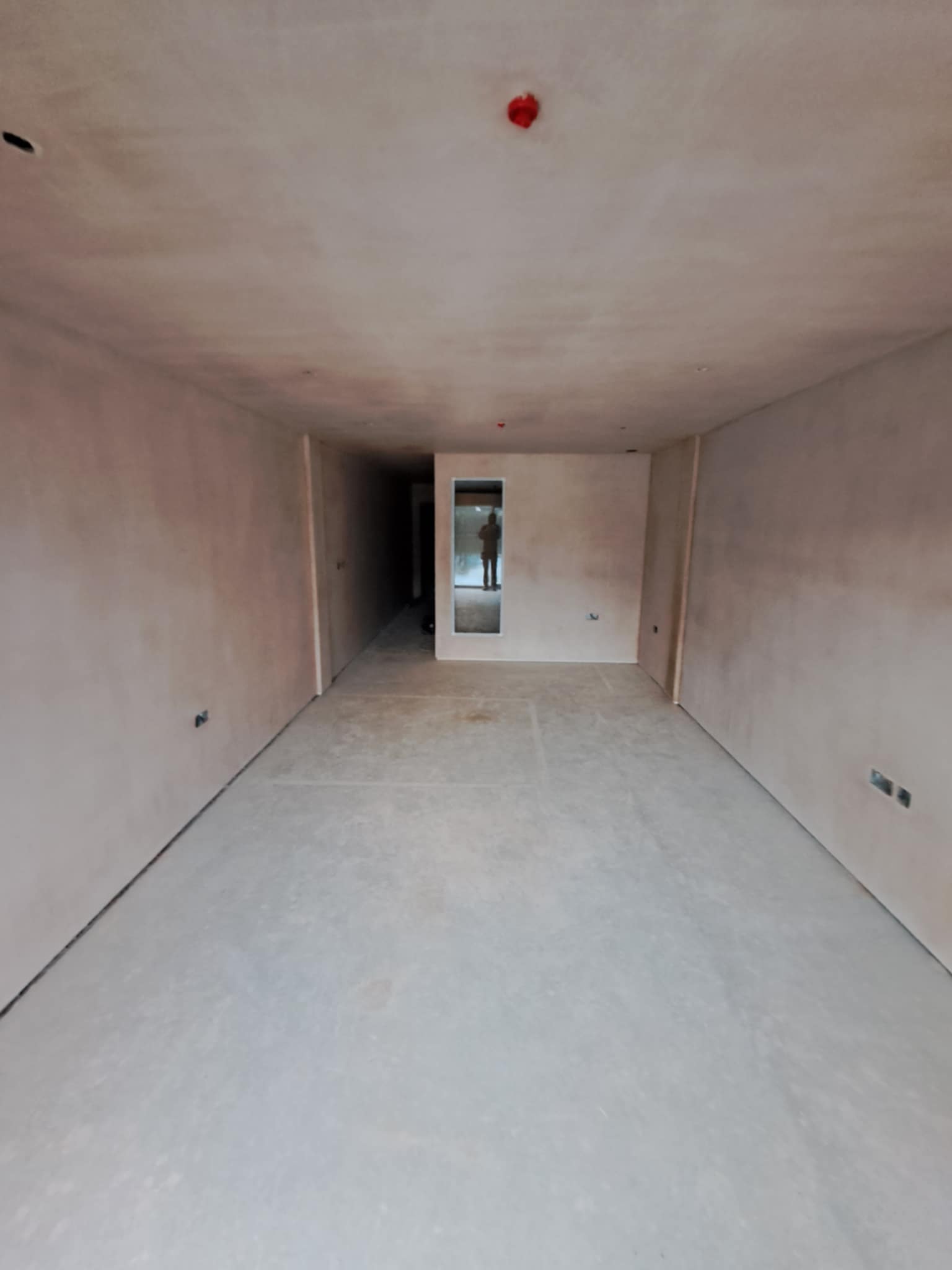 Narrow hallway with new plaster, small window at end, ready for final finishes.