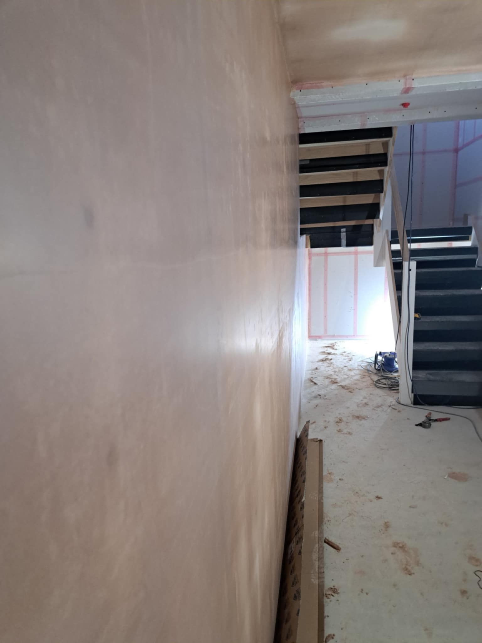 Hallway or landing with new plaster, unfinished floor, stairwell visible.