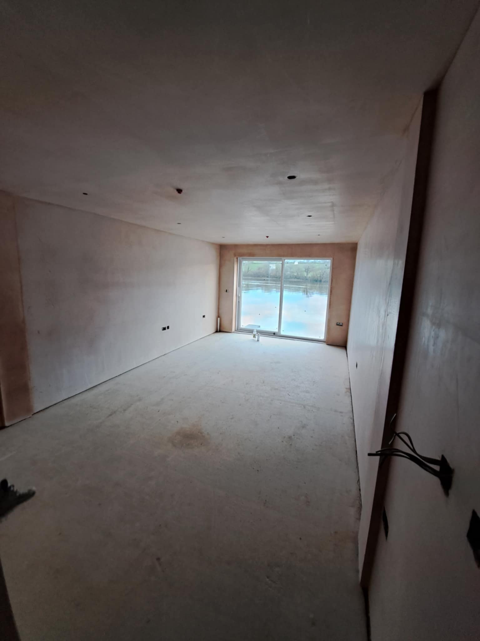 Room with new plaster on walls and ceiling, single window at far end.