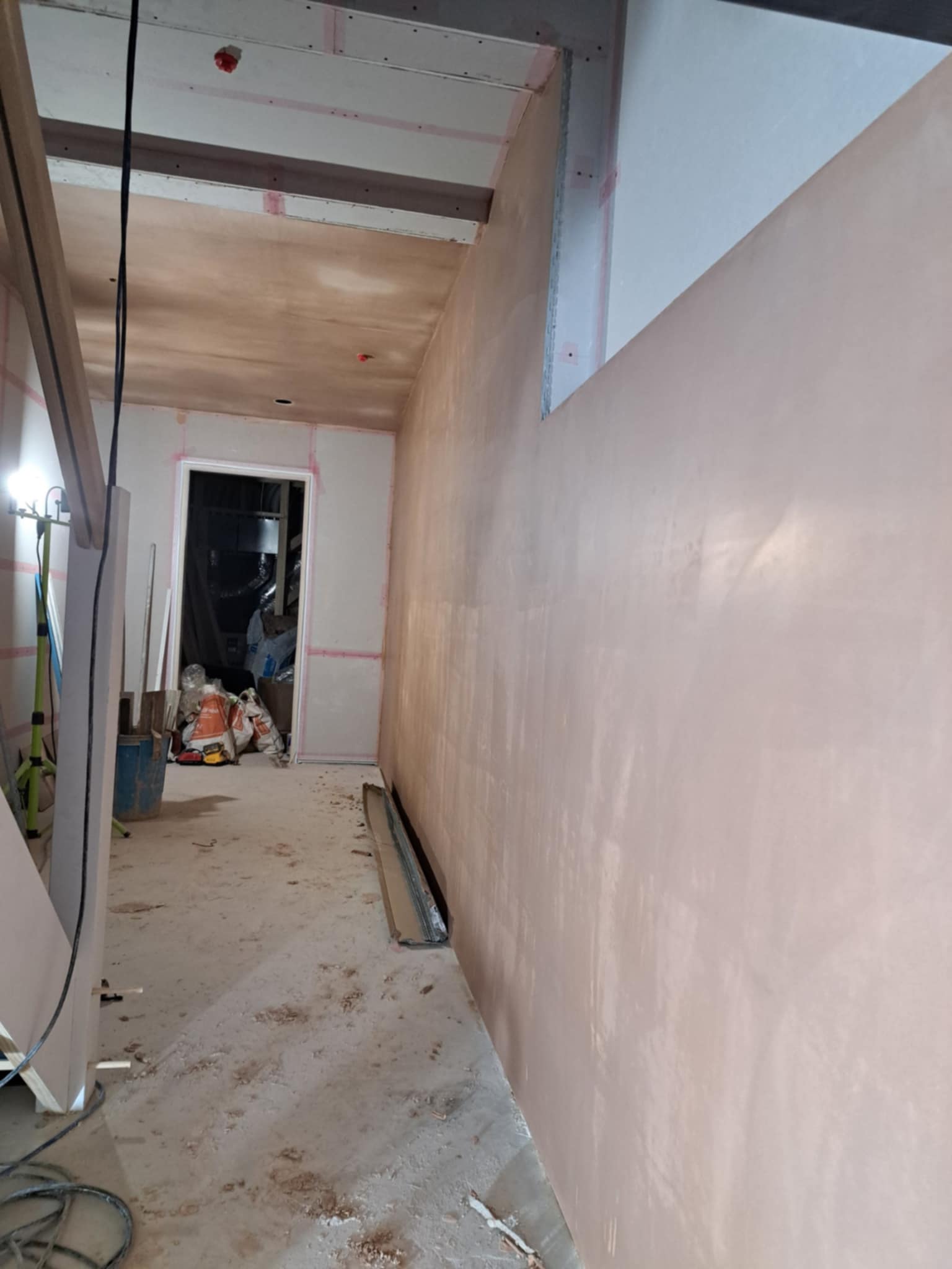 View of a stairwell and hallway with new plaster, some construction debris.