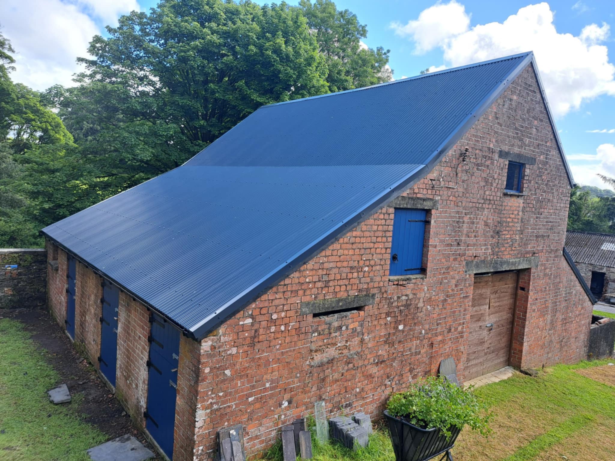 Brick barn with new dark roof, surrounded by trees and grass.