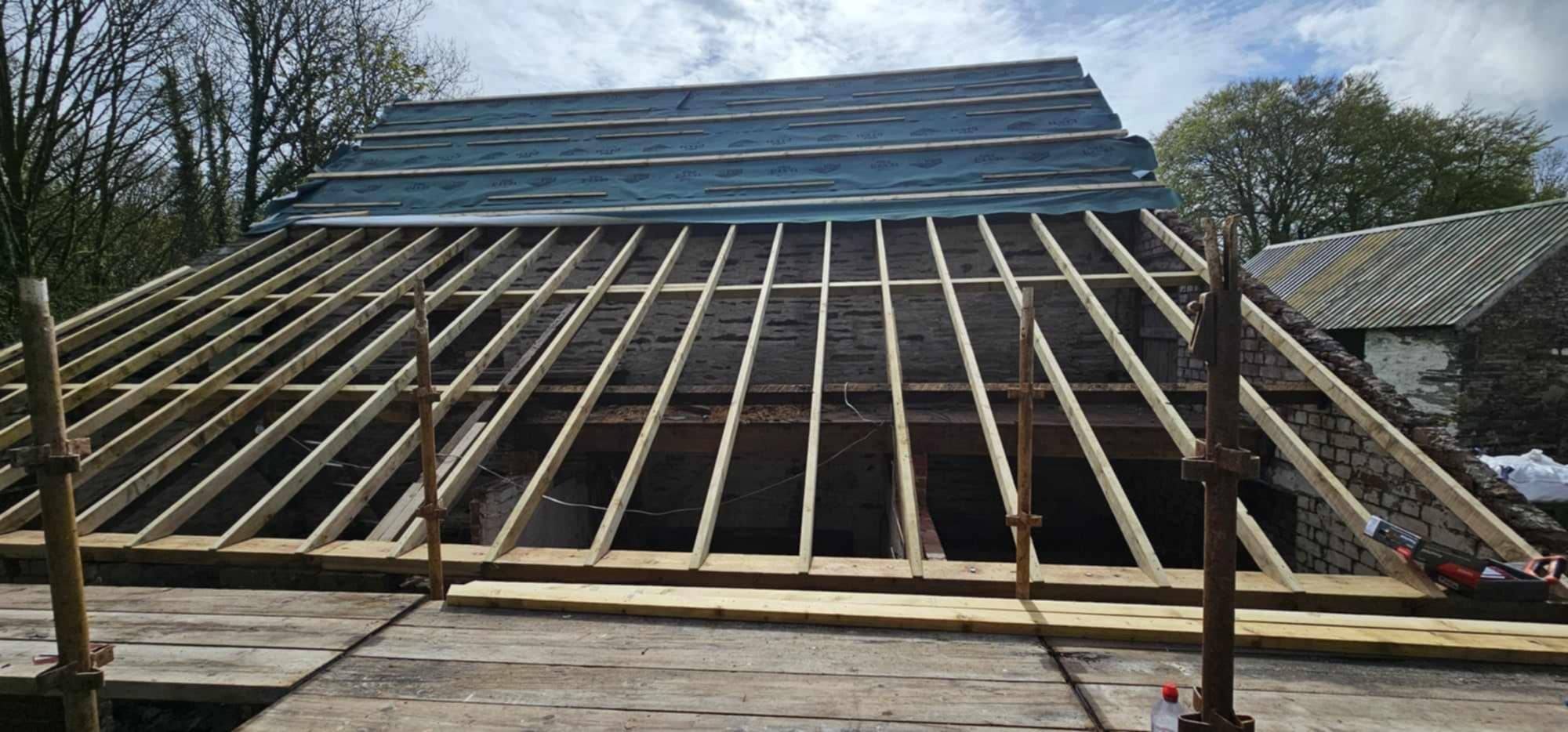 Timber framework for a large roof being installed, blue sky background.