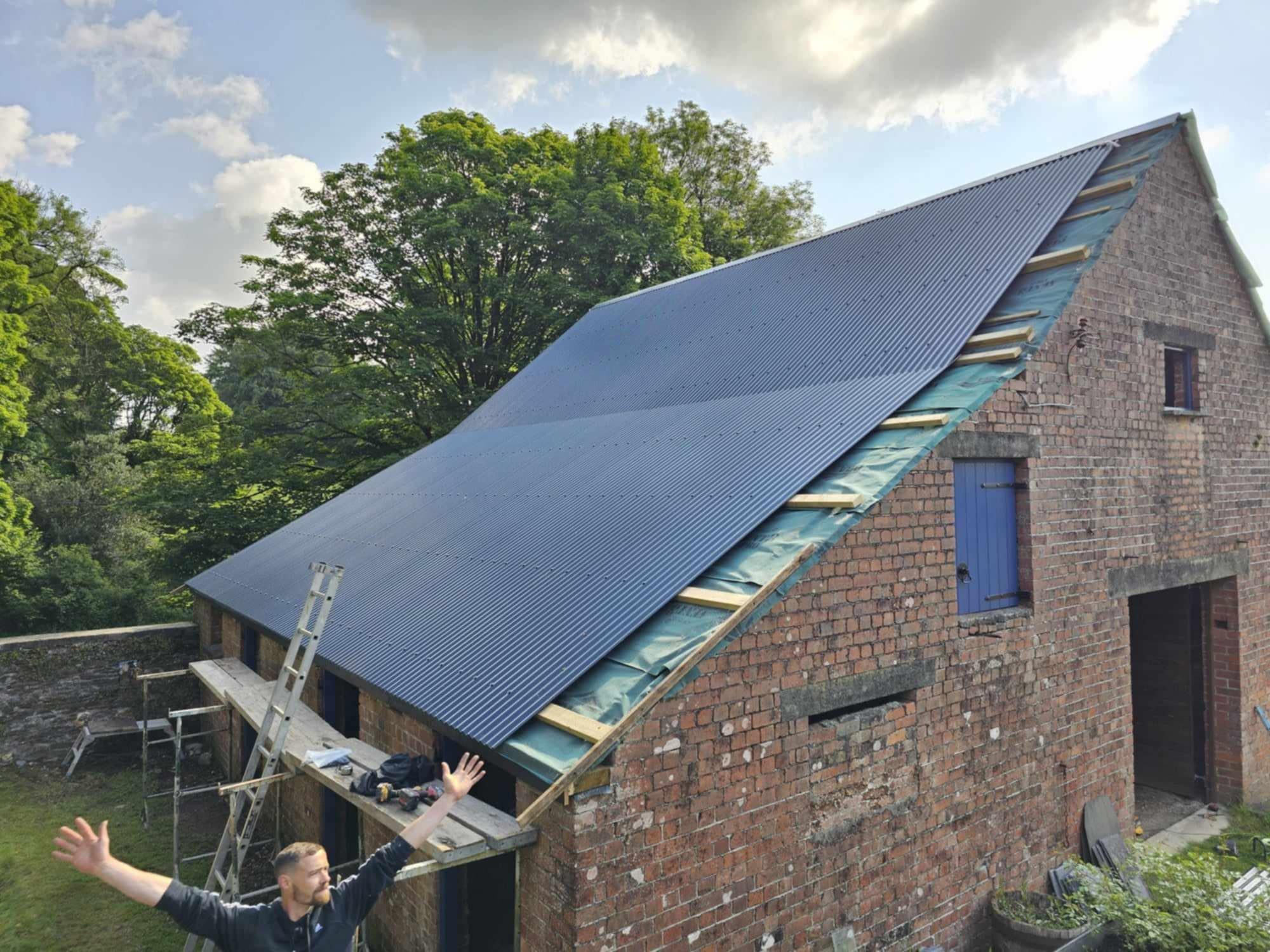 Brick barn with new dark roof sheeting being fitted, side view.