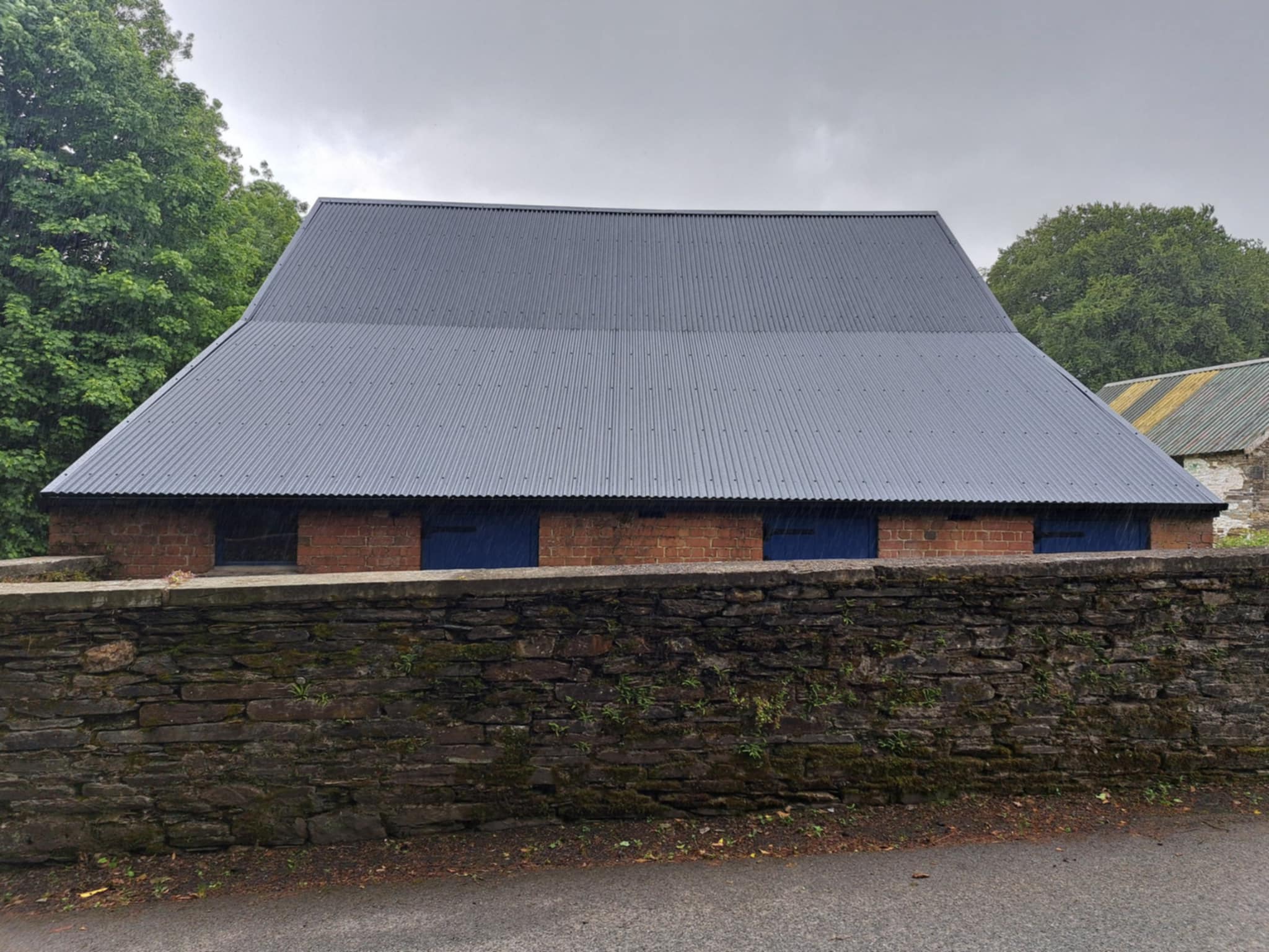 Barn with completed dark roof sheeting, blue sky.