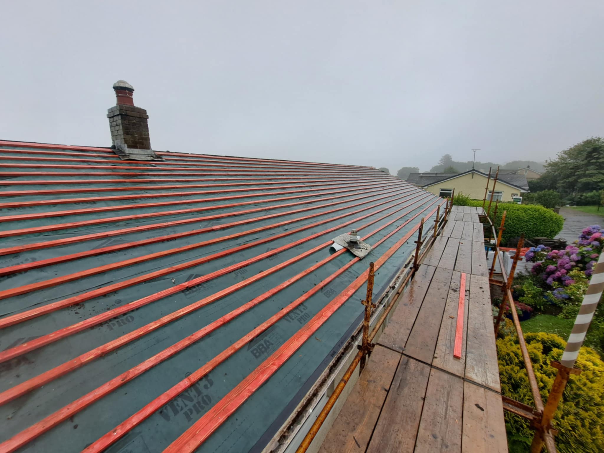 Nearly finished roof, neatly laid slates visible, garden below.