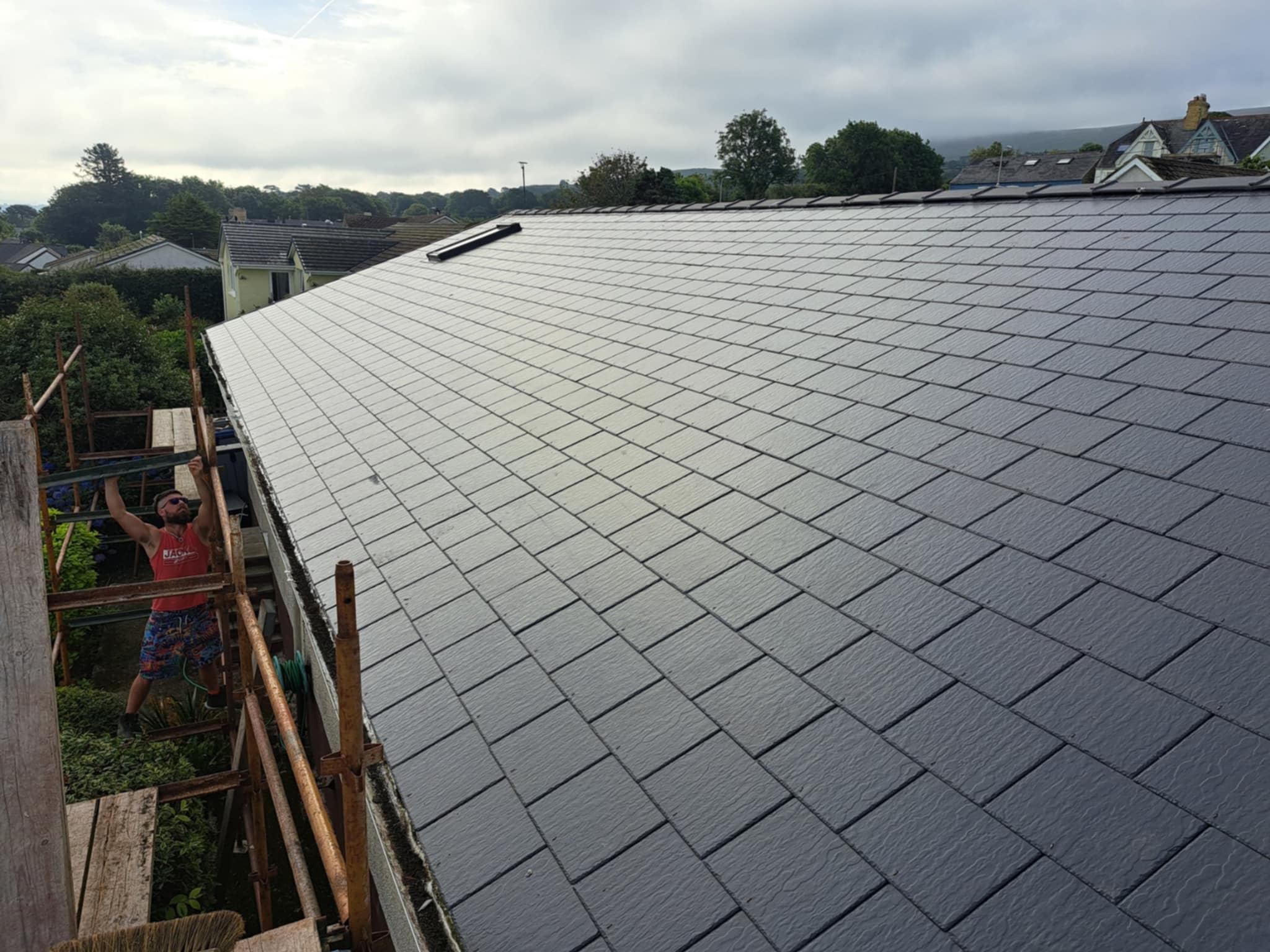 Pitched roof with battens, slate tiles partially fitted, landscape beyond.