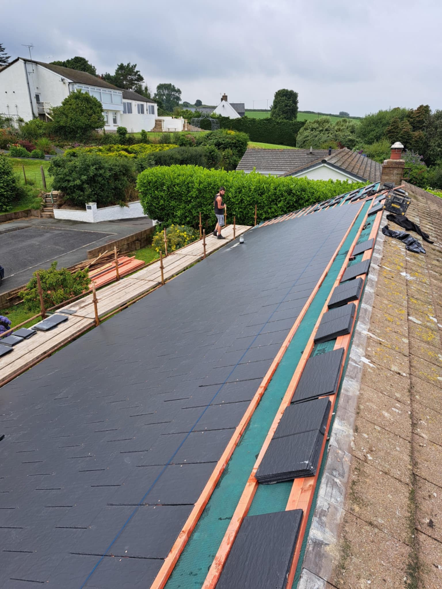 Slate roof with battens and scaffolding, countryside in the distance.
