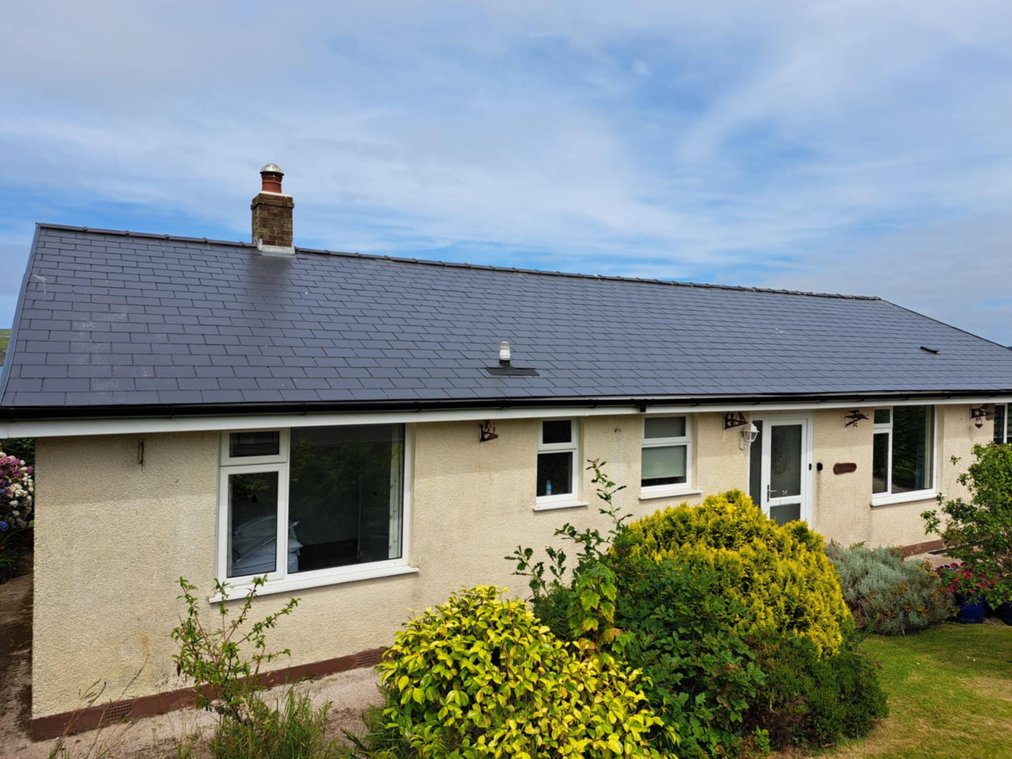 Rear view of a bungalow with new slate roof, garden and hedges.