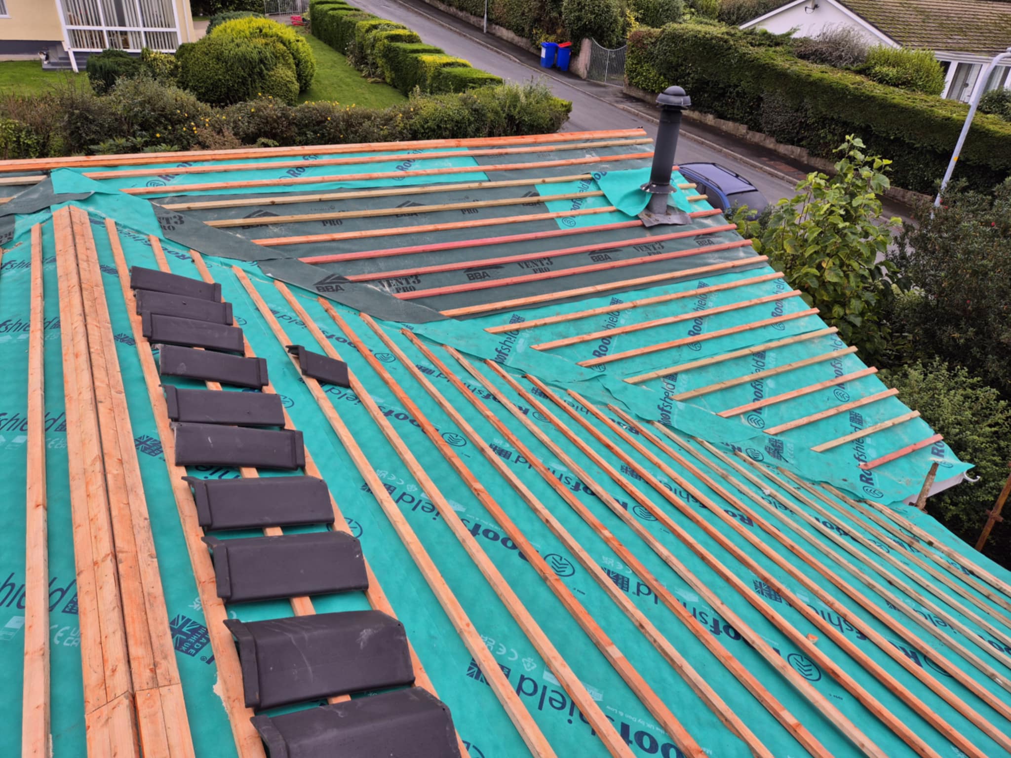 Two people installing green roofing battens on a roof.