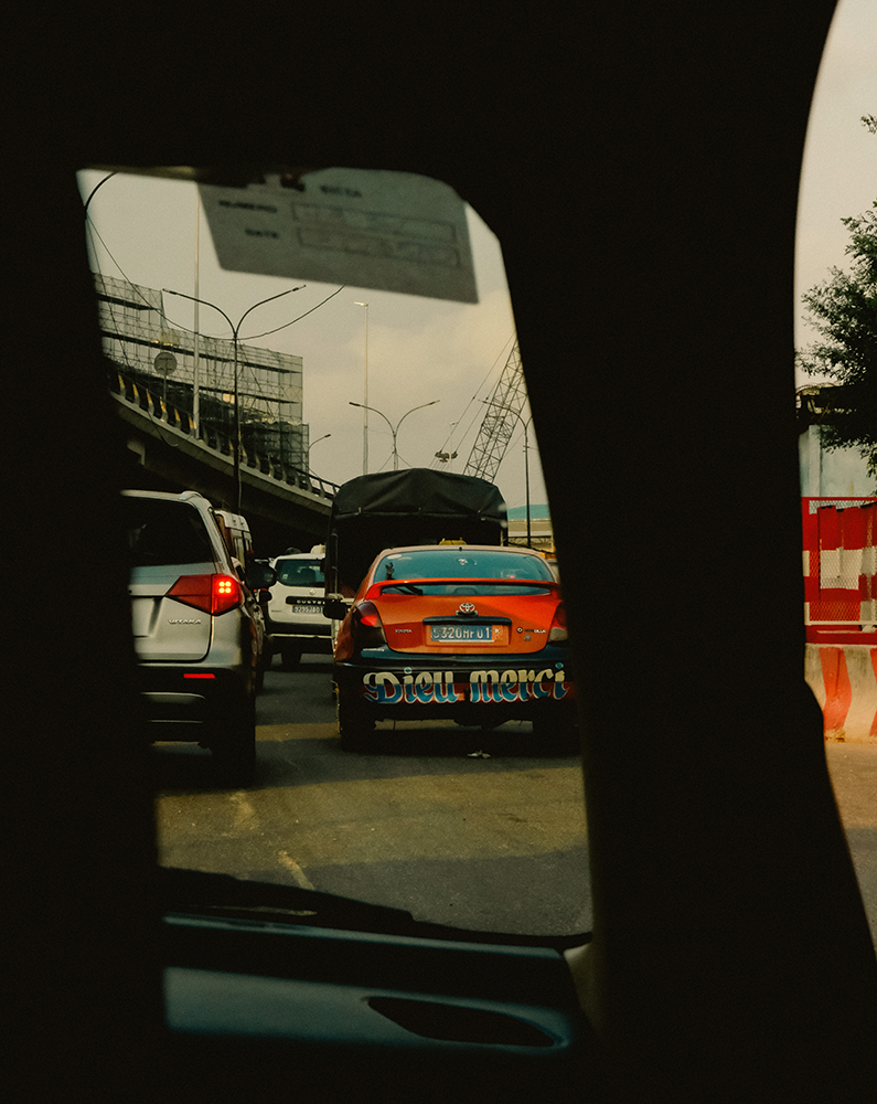 Photographie de Romane Kouo. Voiture avec l'inscription Dieu Merci à l'arrière. 