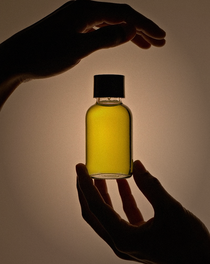 A person holding a small bottle of oil, showcasing the bottle's label and the person's hand.