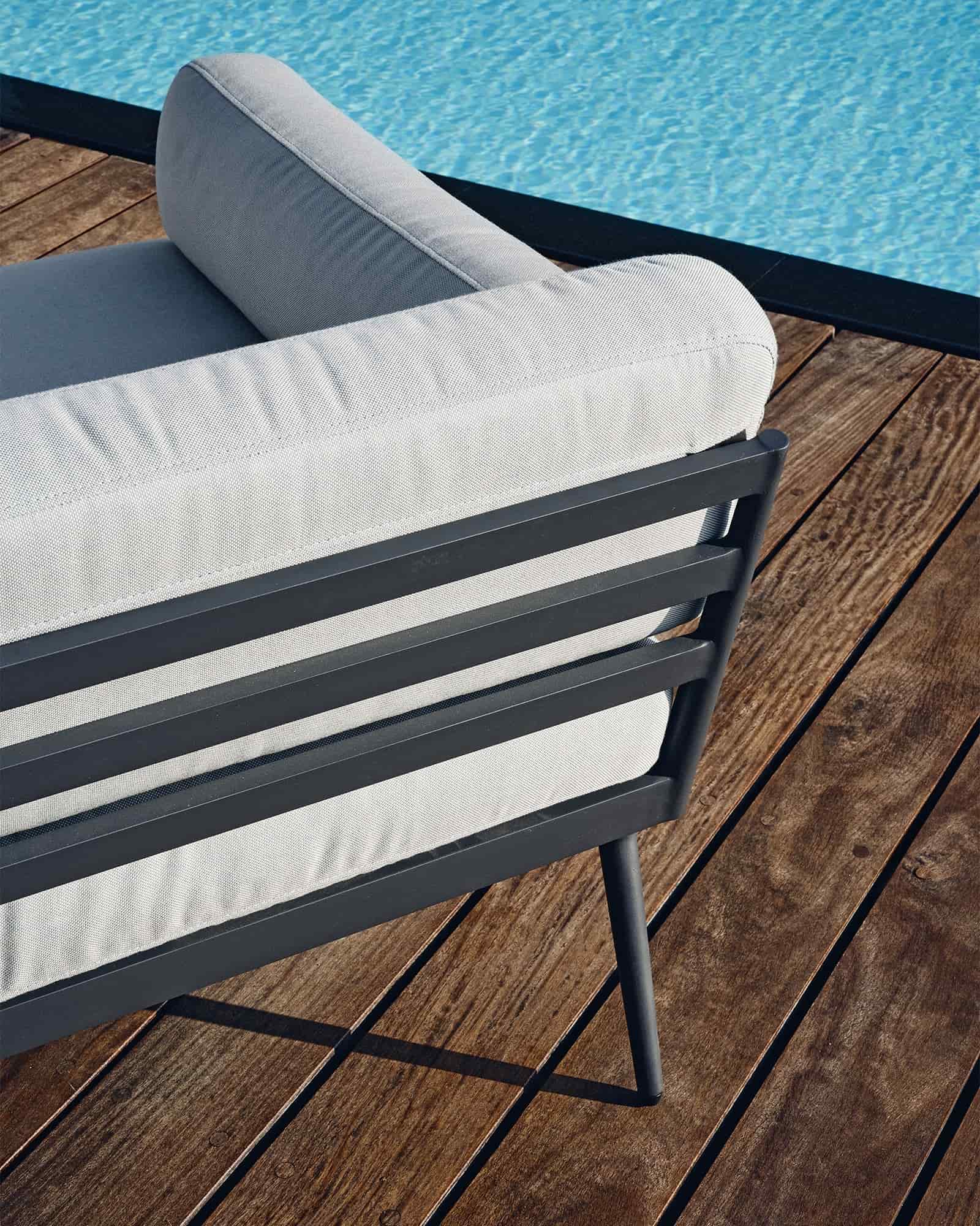 Close up of Skargaarden Anholt sofa lounge with light grey cushions and black metal frame on wooden deck beside a pool represented by Terentti