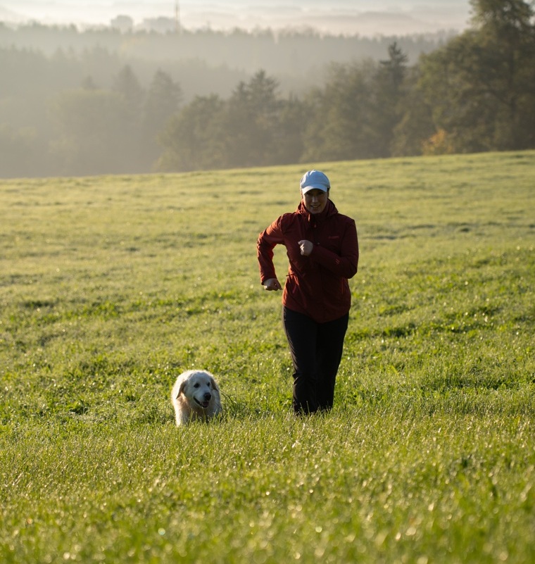 Doris und Jacky nebeneinander beim Laufen auf einer Straße mit Wiese und Bäumen im Hintergrund.