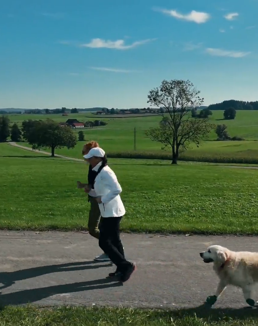 Doris läuft mit ihrer Schülerin und Jacky folgt in grüner Landschaft auf einer Straße