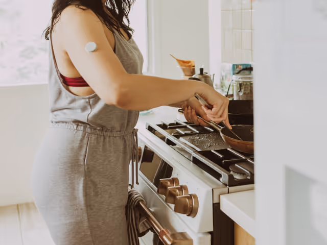 Frau mit Insulinsensor am Arm und Lipödem-Beinen steht am Herd und kocht