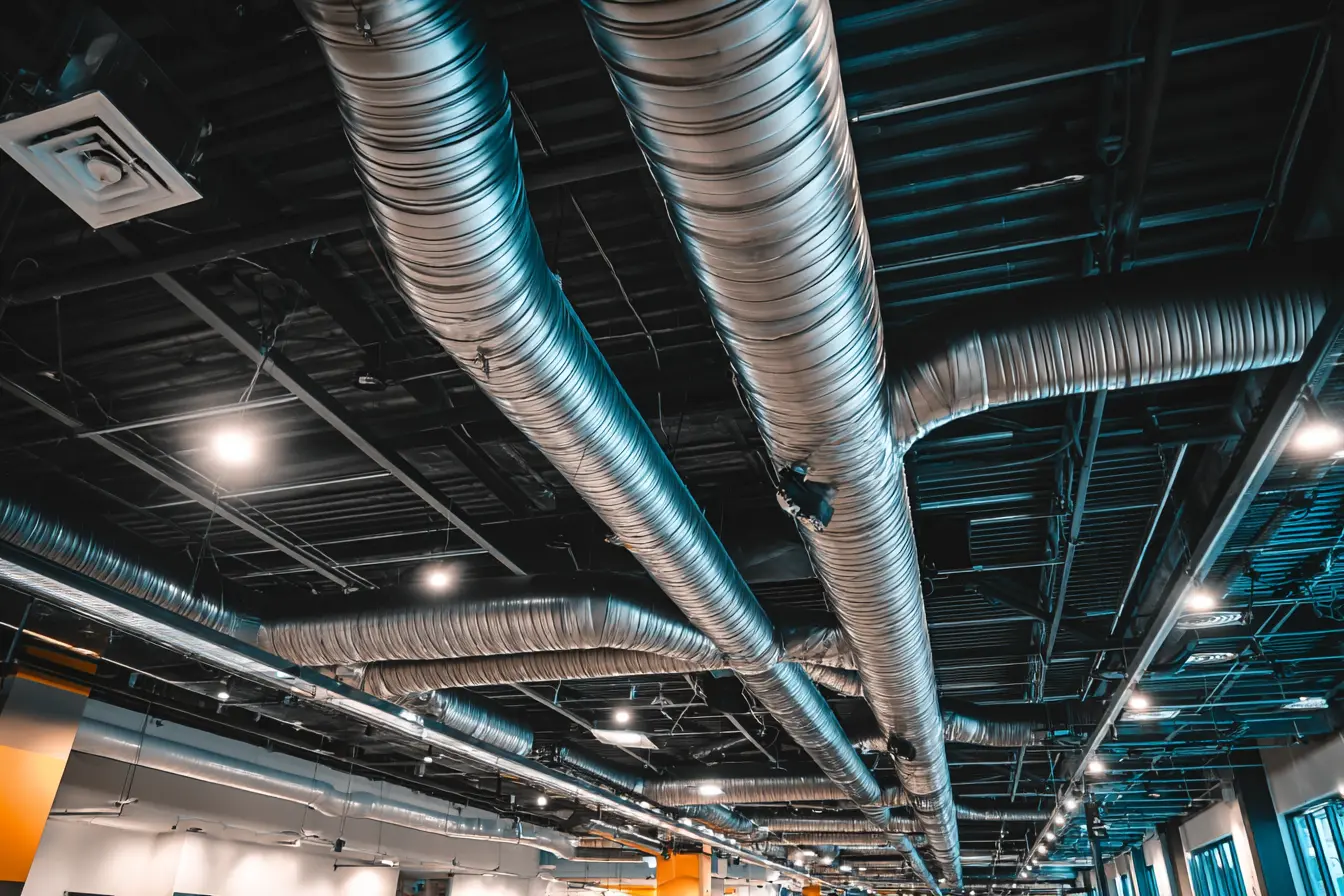 Industrial commercial HVAC ductwork installation inside a large building with exposed spiral ducts, ventilation diffusers, and ceiling-mounted systems, realistic lighting, high detail, modern mechanical infrastructure