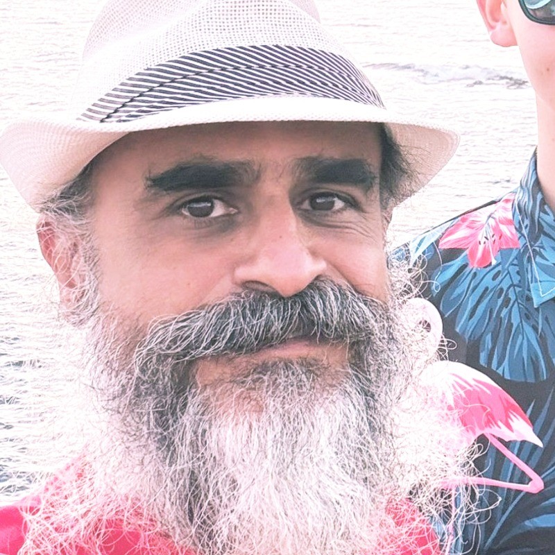 Close-up of a man with a long grey beard and mustache wearing a white hat with a black striped band.