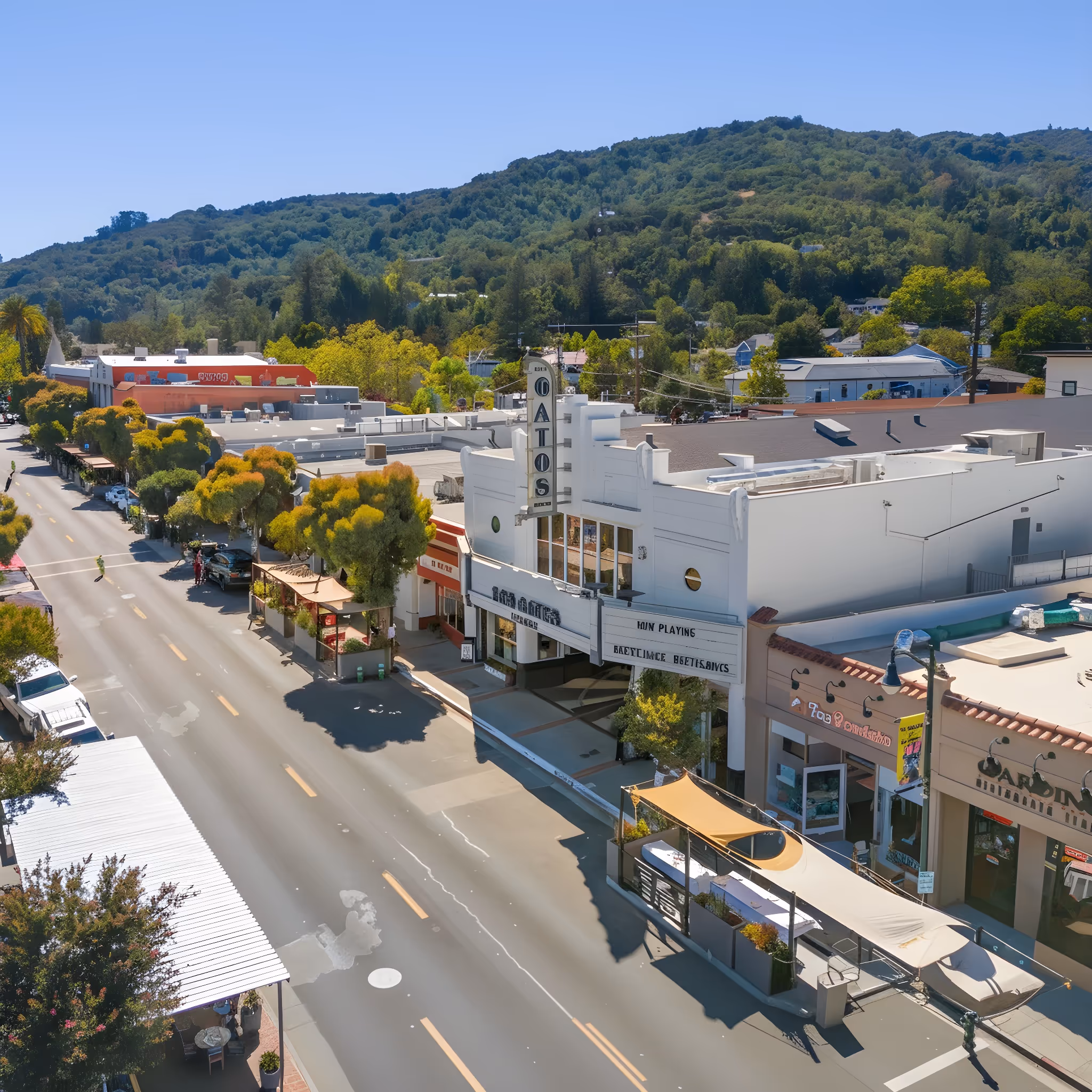Aerial view of downtown Los Gatos with the historic Los Gatos Theater and surrounding shops along a tree-lined street with hills in the background.