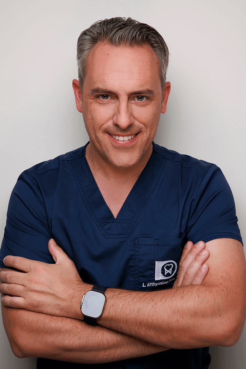 Man with short gray hair in navy blue medical scrubs smiling with arms crossed.