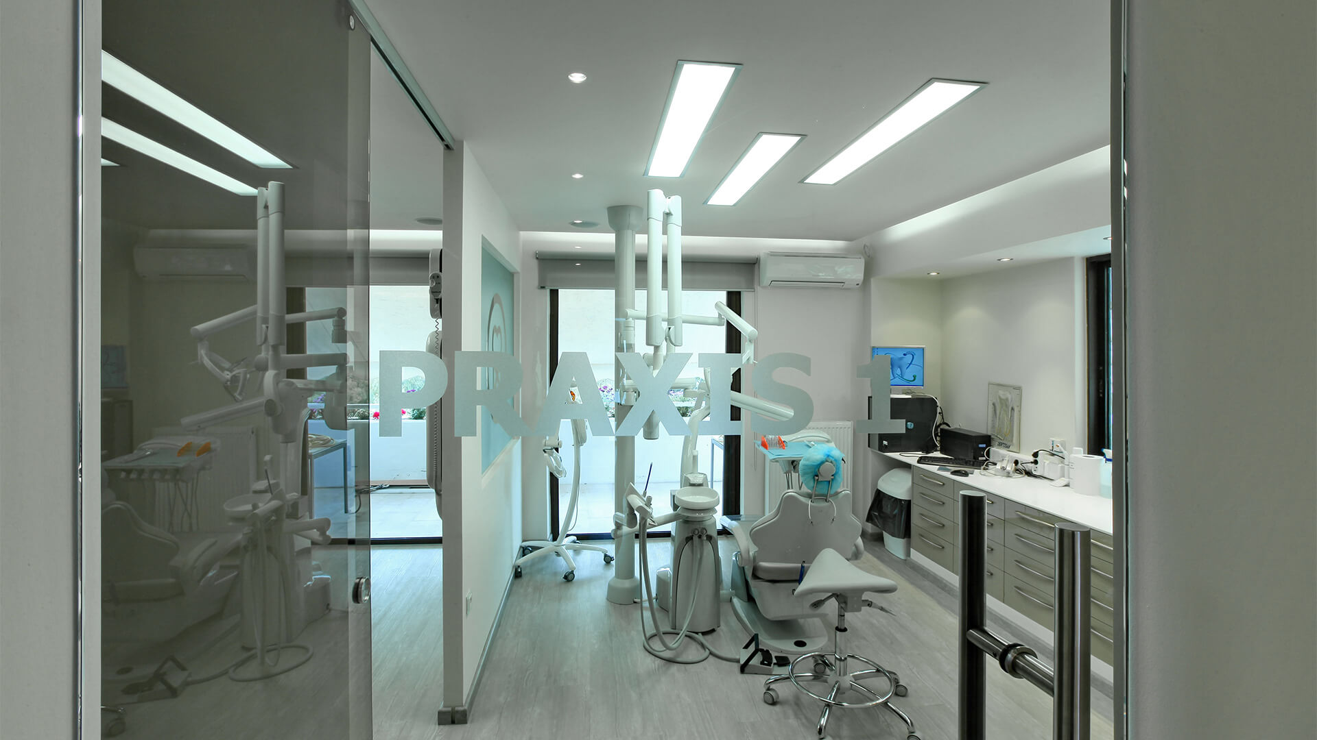 Modern dental clinic room with a dental chair, equipment, and cabinets visible through glass door labeled PRAXIS 1.
