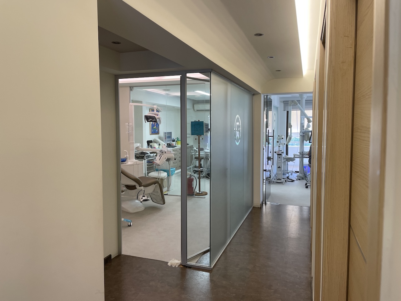 Hallway leading to modern dental clinics with glass partitions and dental chairs visible inside.