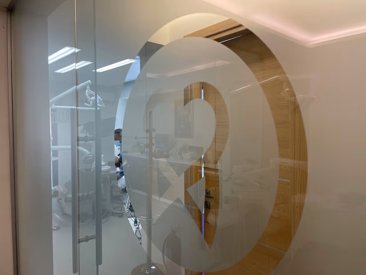 View through frosted glass door with a dental logo into a dentist's office showing a dentist wearing a mask inside.