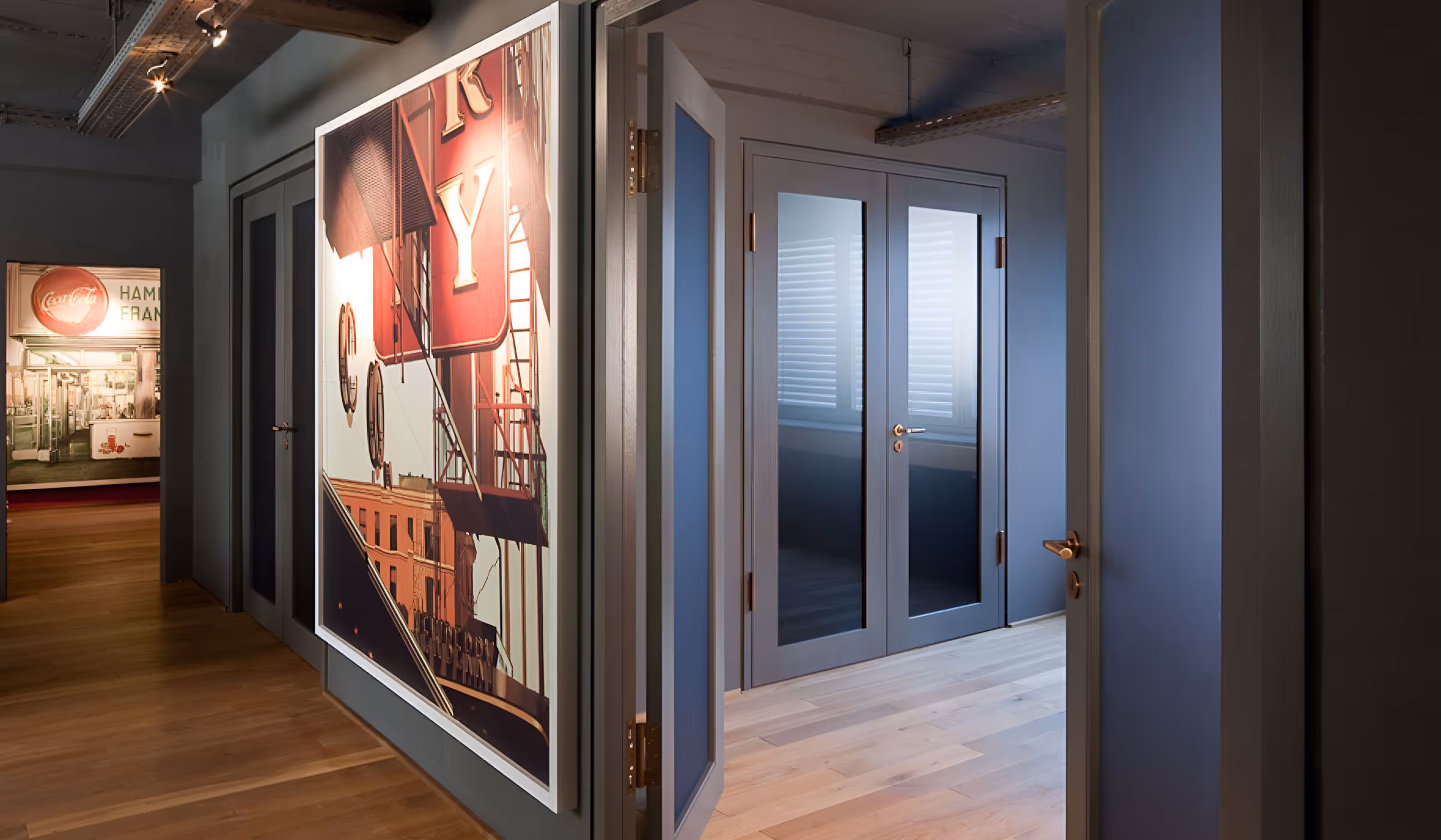 Moderner Büroflur mit großformatigen Stadtfotografien an den Wänden, grauen Türen und hellem Holzboden.