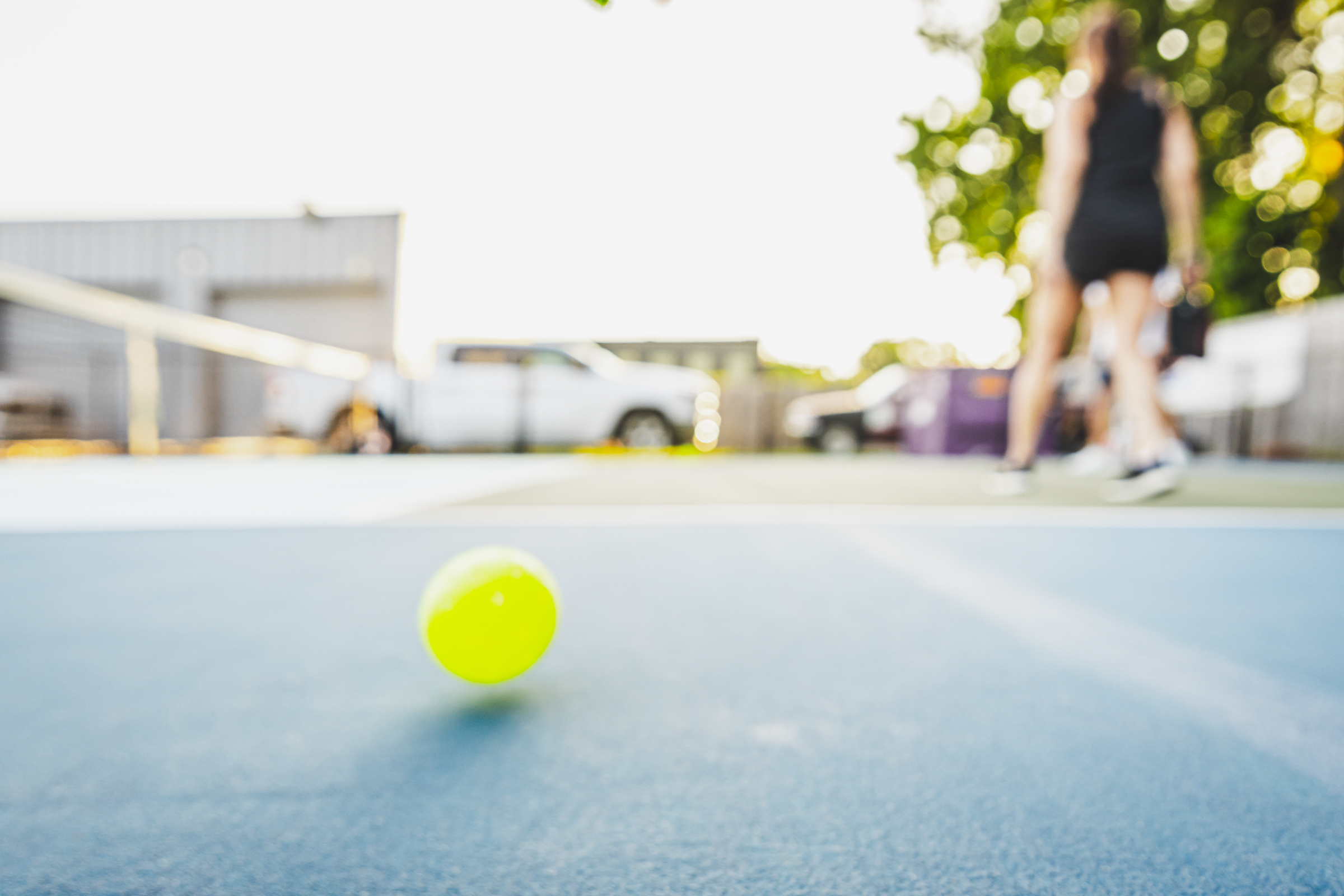 Pickleball lying on a pickleball court with a player in the background