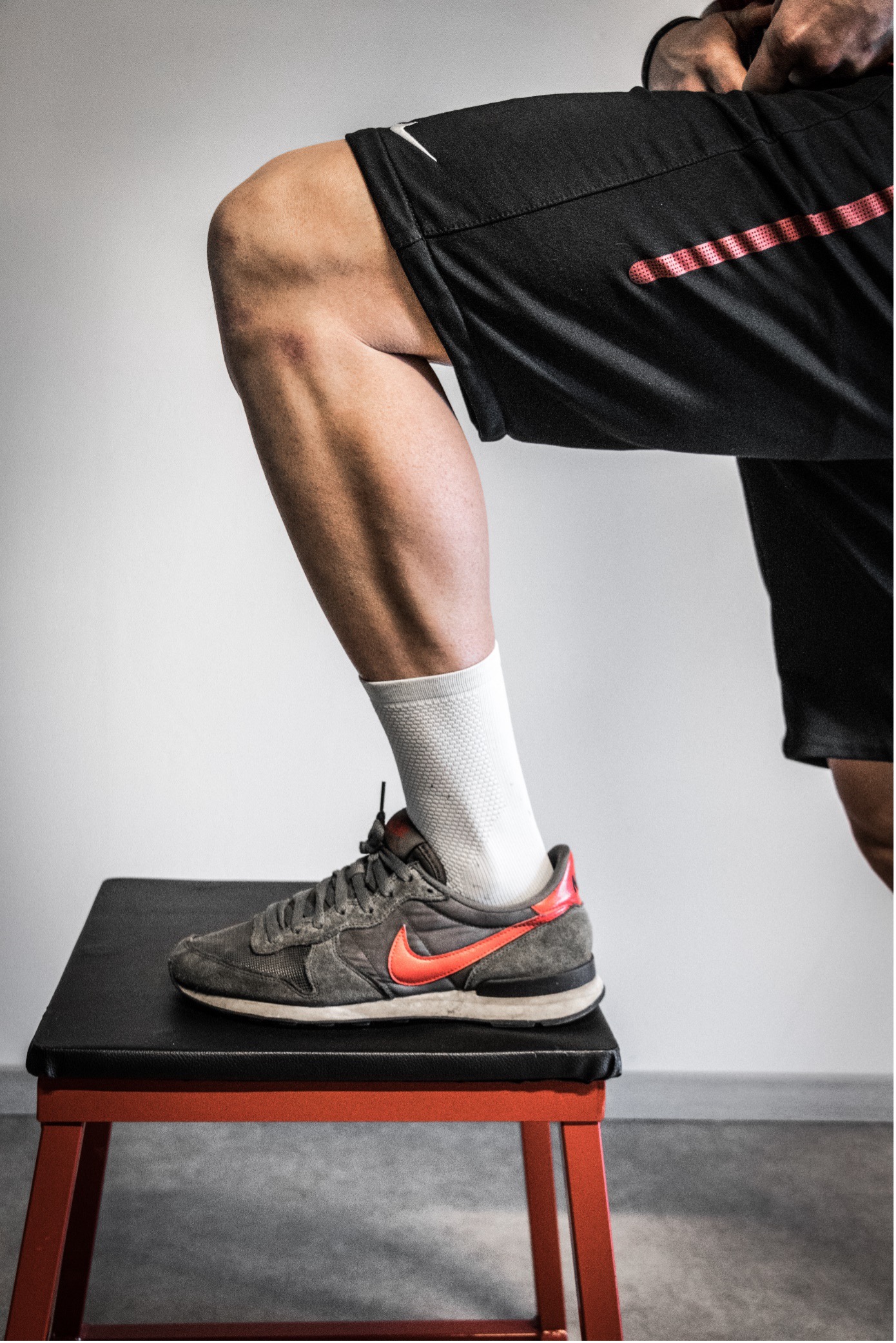 Gestrekte mannenbeen met witte sok en grijze Nike sneaker op een rood fitnessbankje.