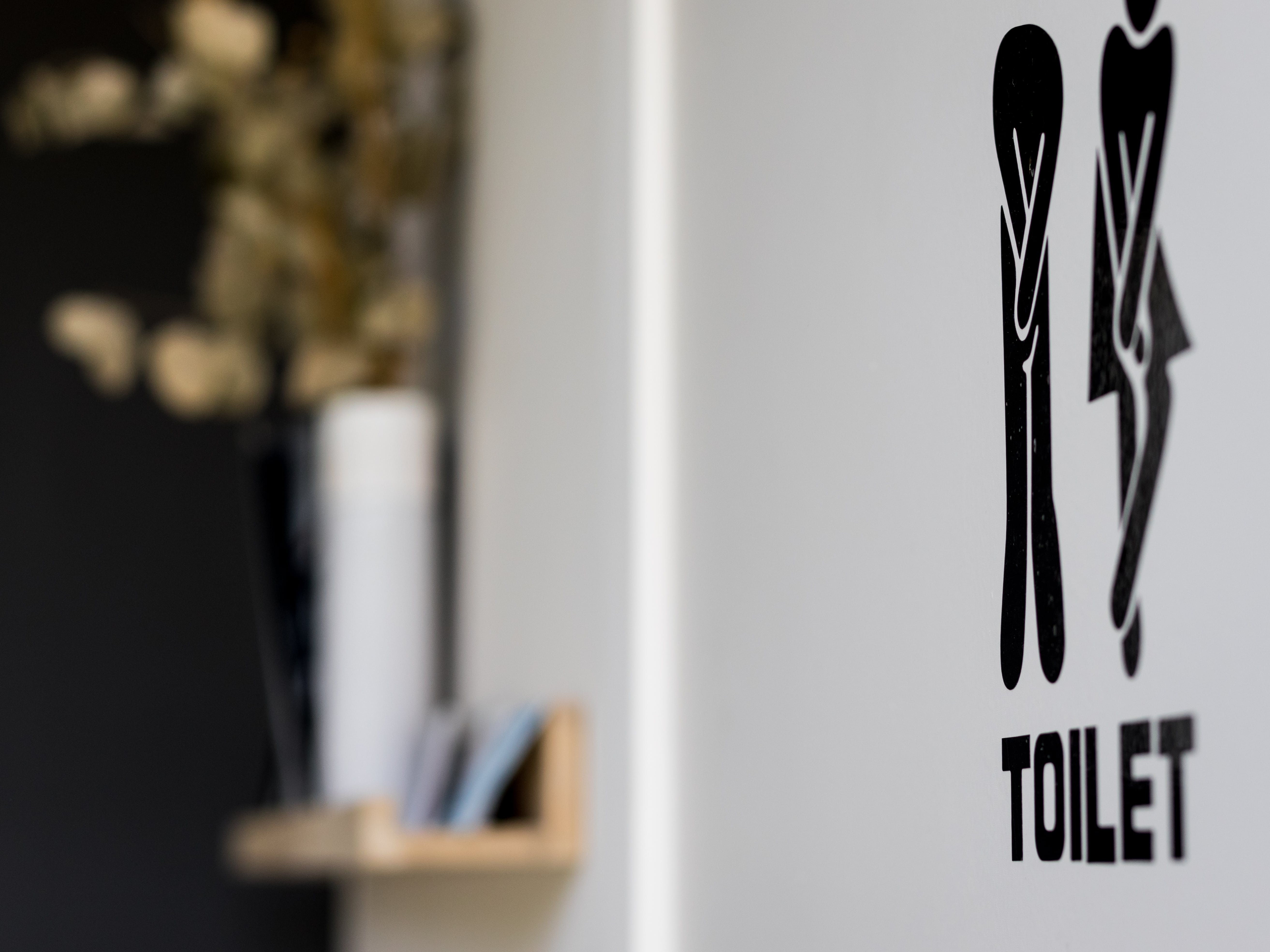 Pictogram van mannelijke en vrouwelijke toiletten op een grijze muur, met een onscherpe achtergrond van een plank en decoratie.