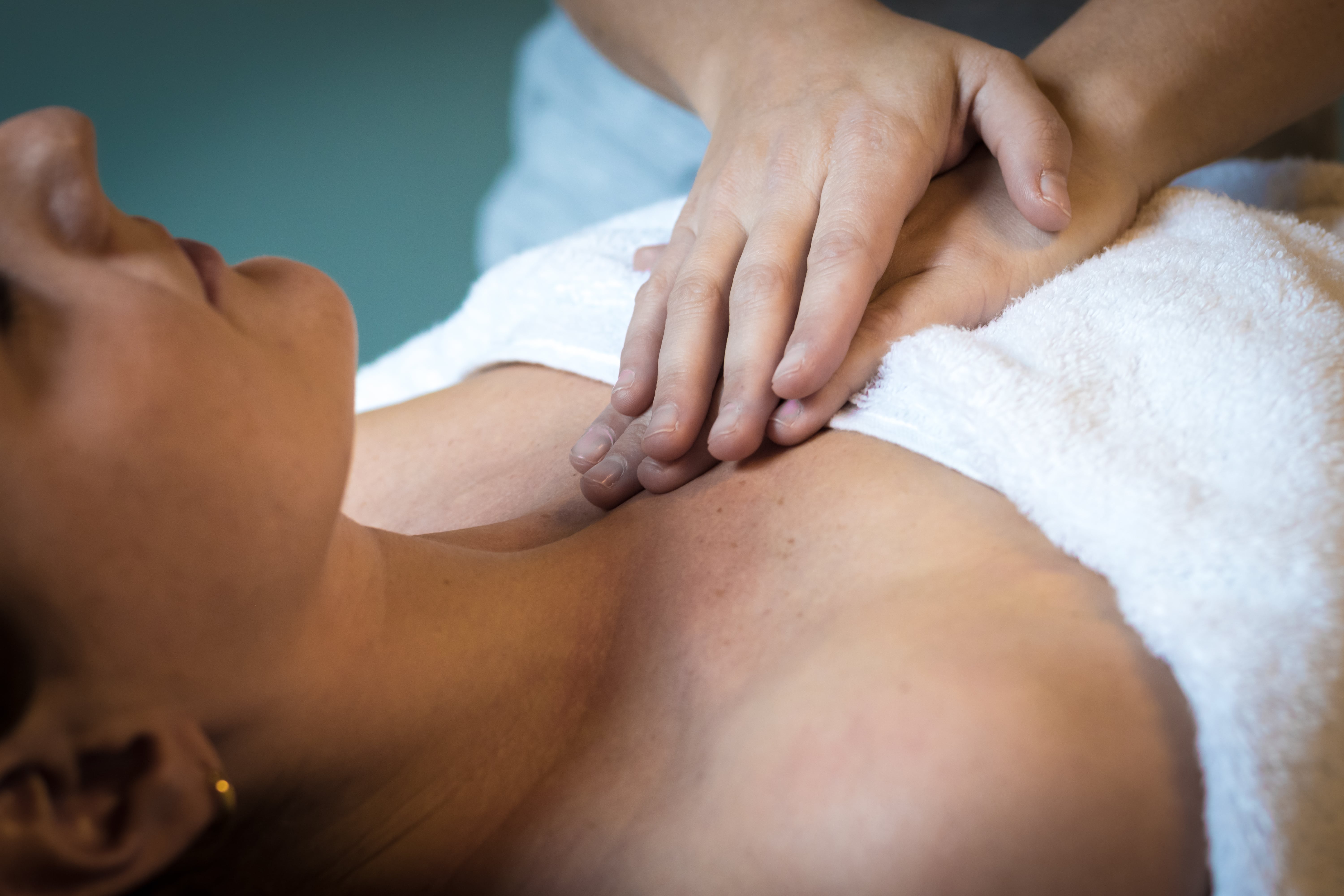Handen die zachte massage geven op de borstkas van een persoon bedekt met een witte doek.
