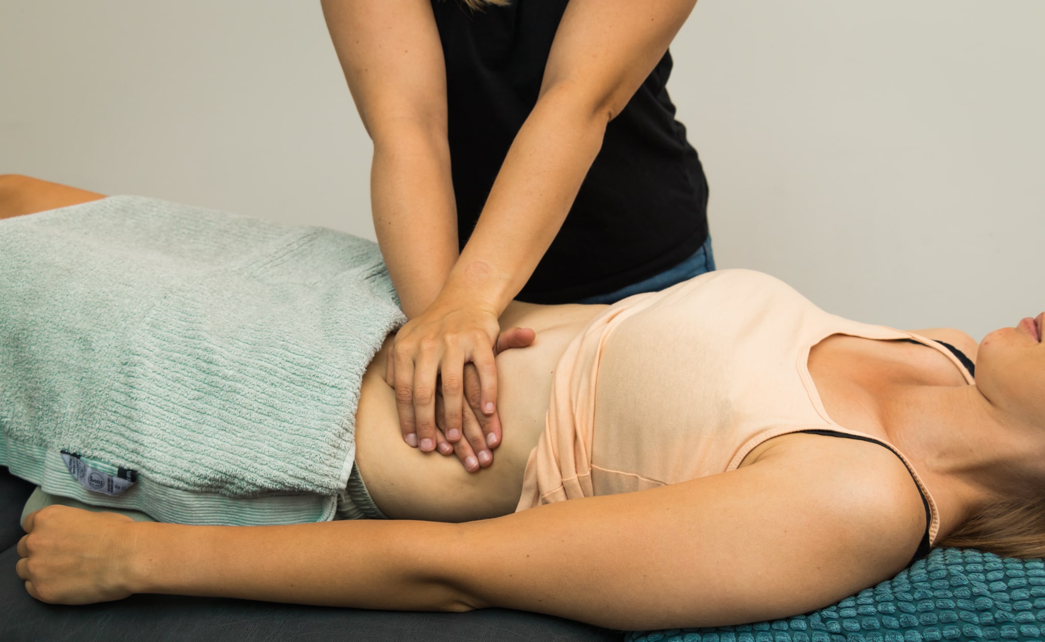 Een persoon die een buikmassage geeft aan een liggende vrouw met een handdoek op haar onderlichaam.