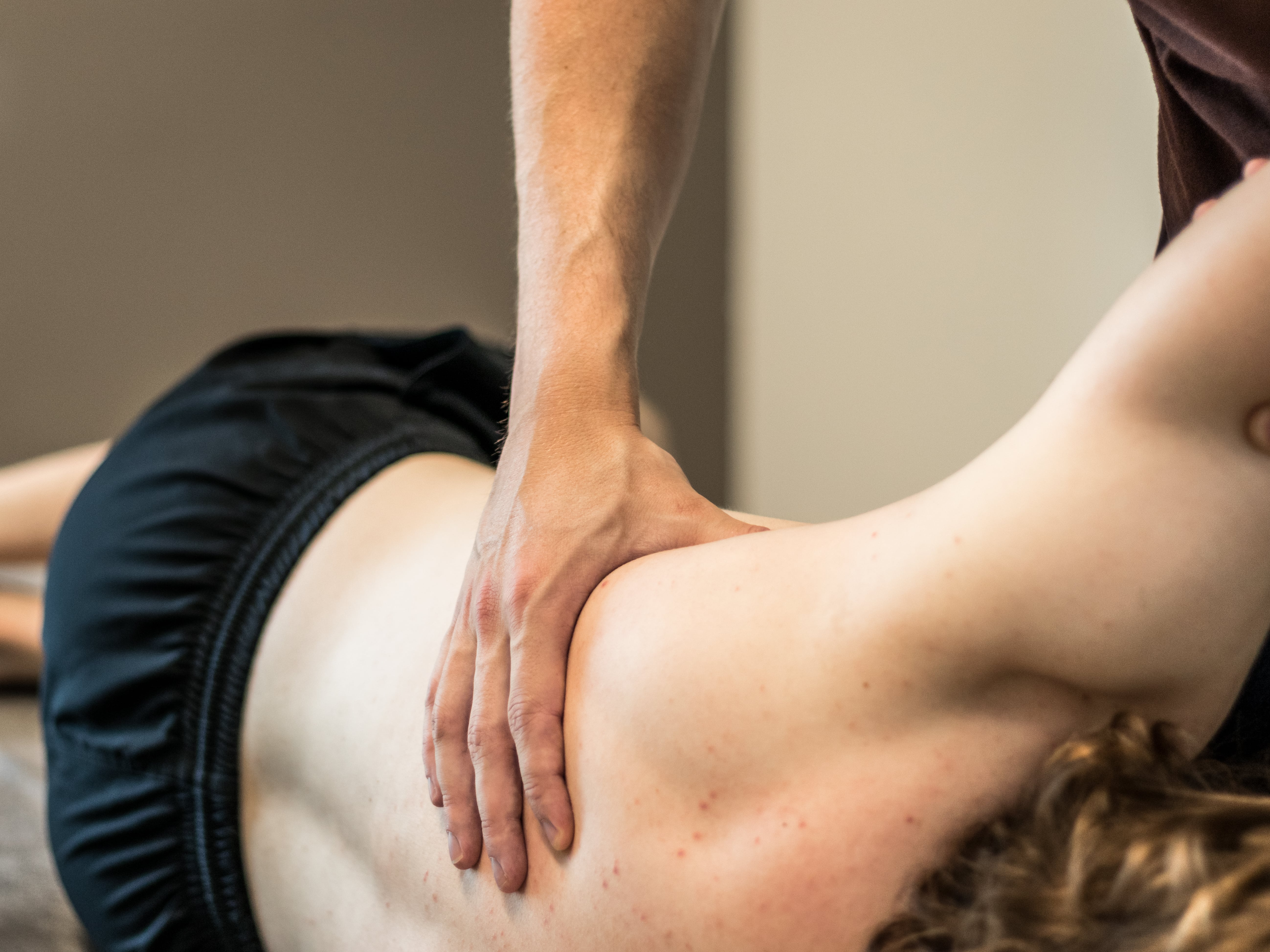 Hand van een therapeut die de onderrug van een persoon die op zijn zij ligt masseert.