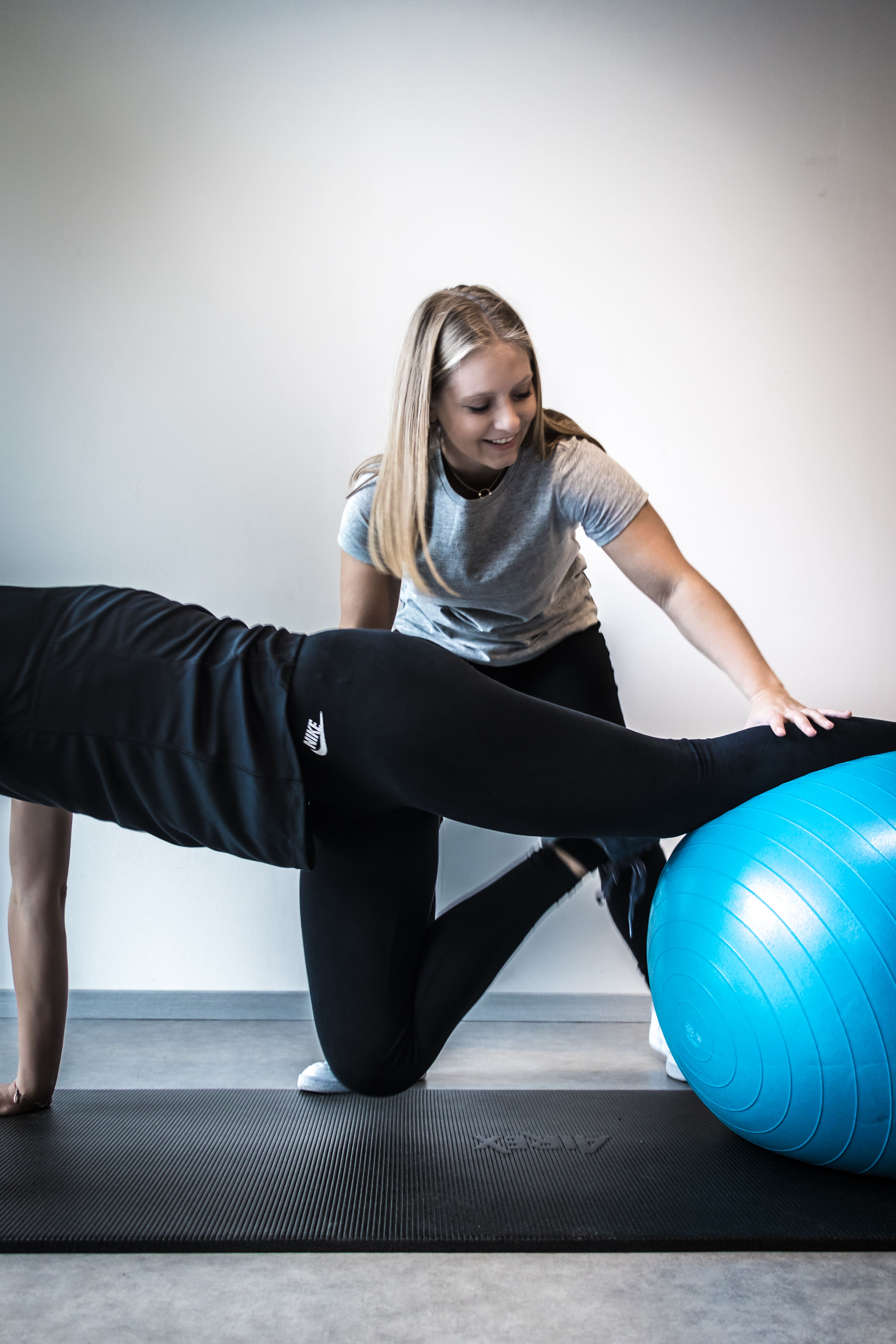 Persoon die een oefening doet met een blauwe fitnessbal terwijl een trainer helpt.