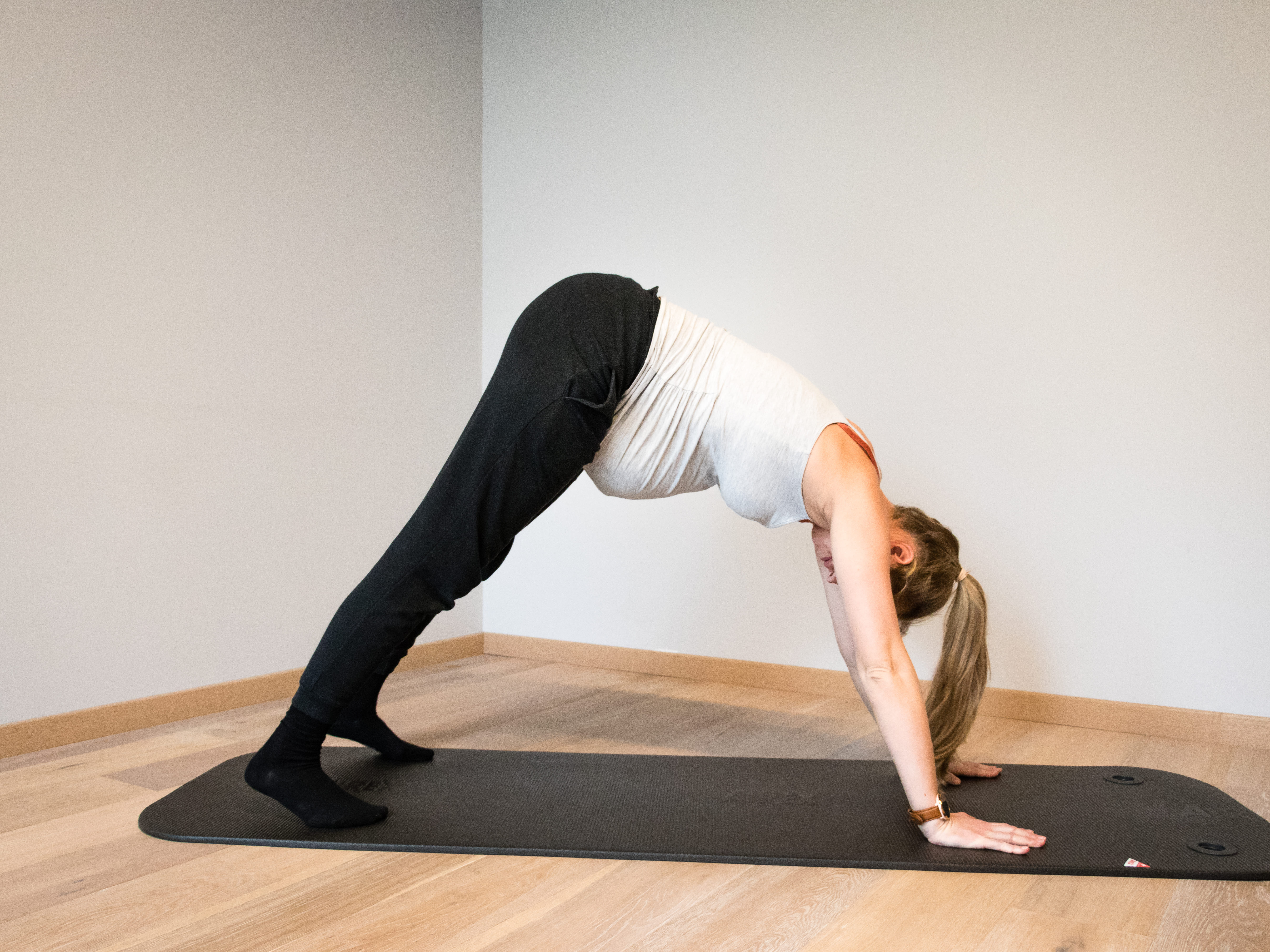 Vrouw in sportkleding doet yoga-oefening op mat in een lege kamer met houten vloer.