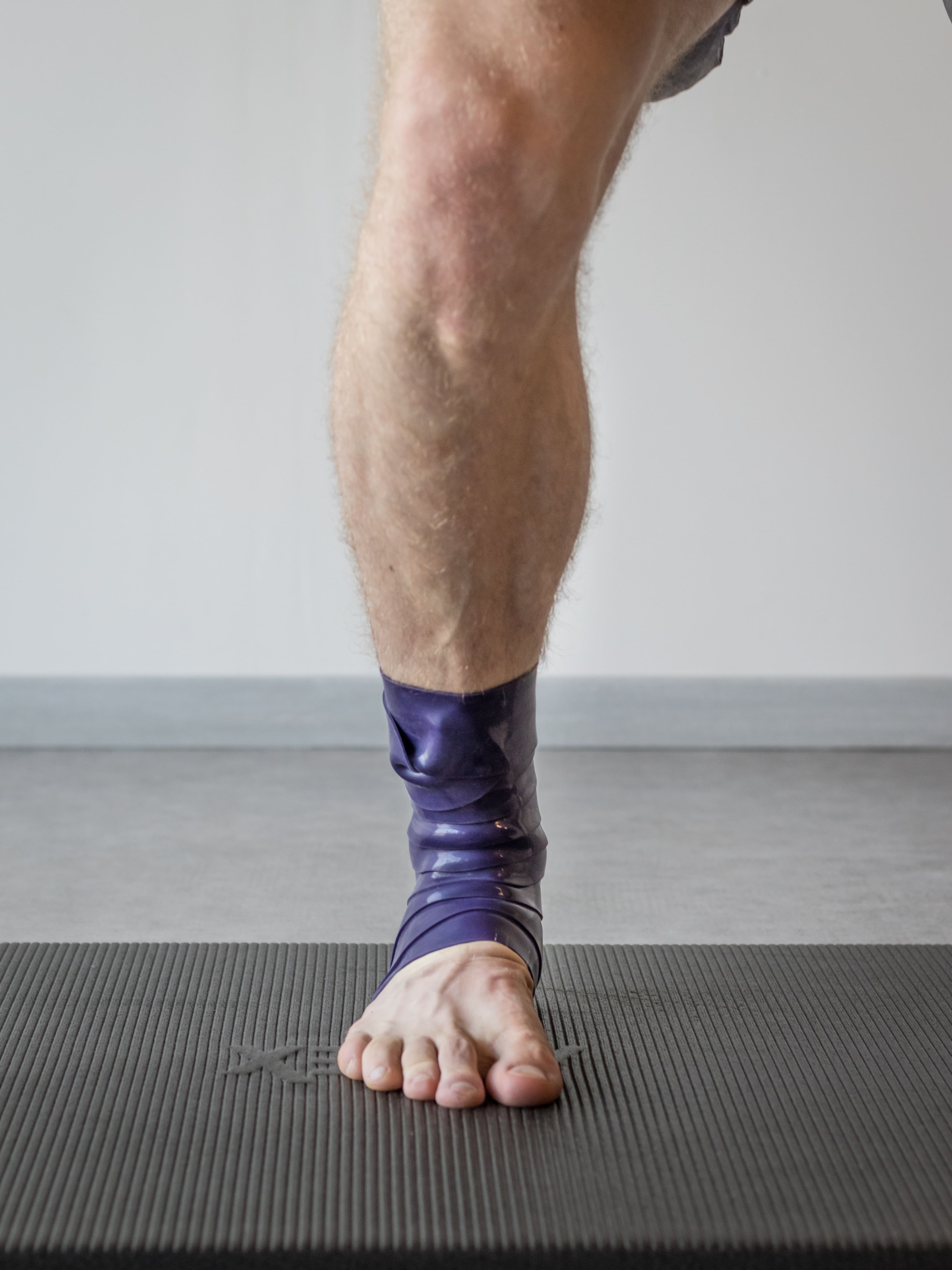 Een been met een paarse elastische bandage rond de enkel, staand op een sportmat.