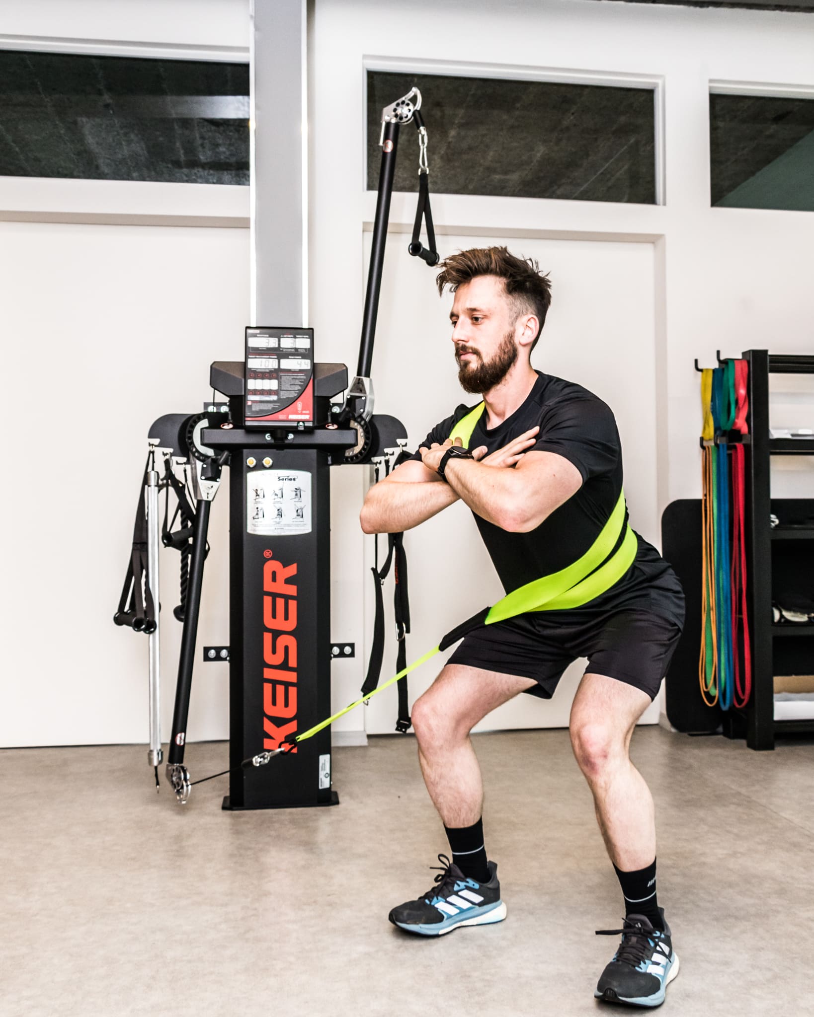 Man die squattoefening doet met weerstandsbanden bevestigd aan een fitnessapparaat in een sportschool.