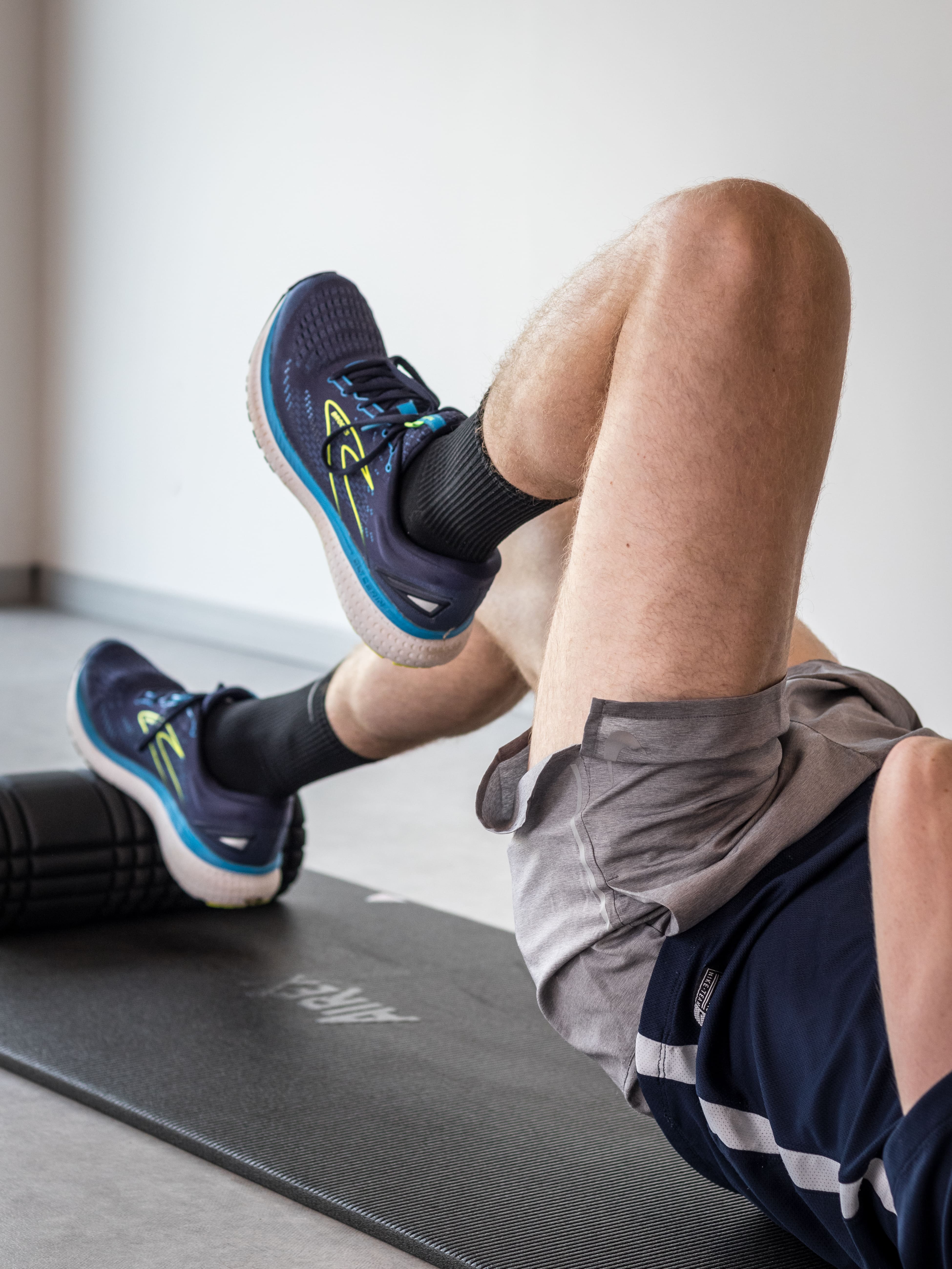 Persoon die een foam roller gebruikt voor het uitrollen van de kuitspieren op een zwarte mat.